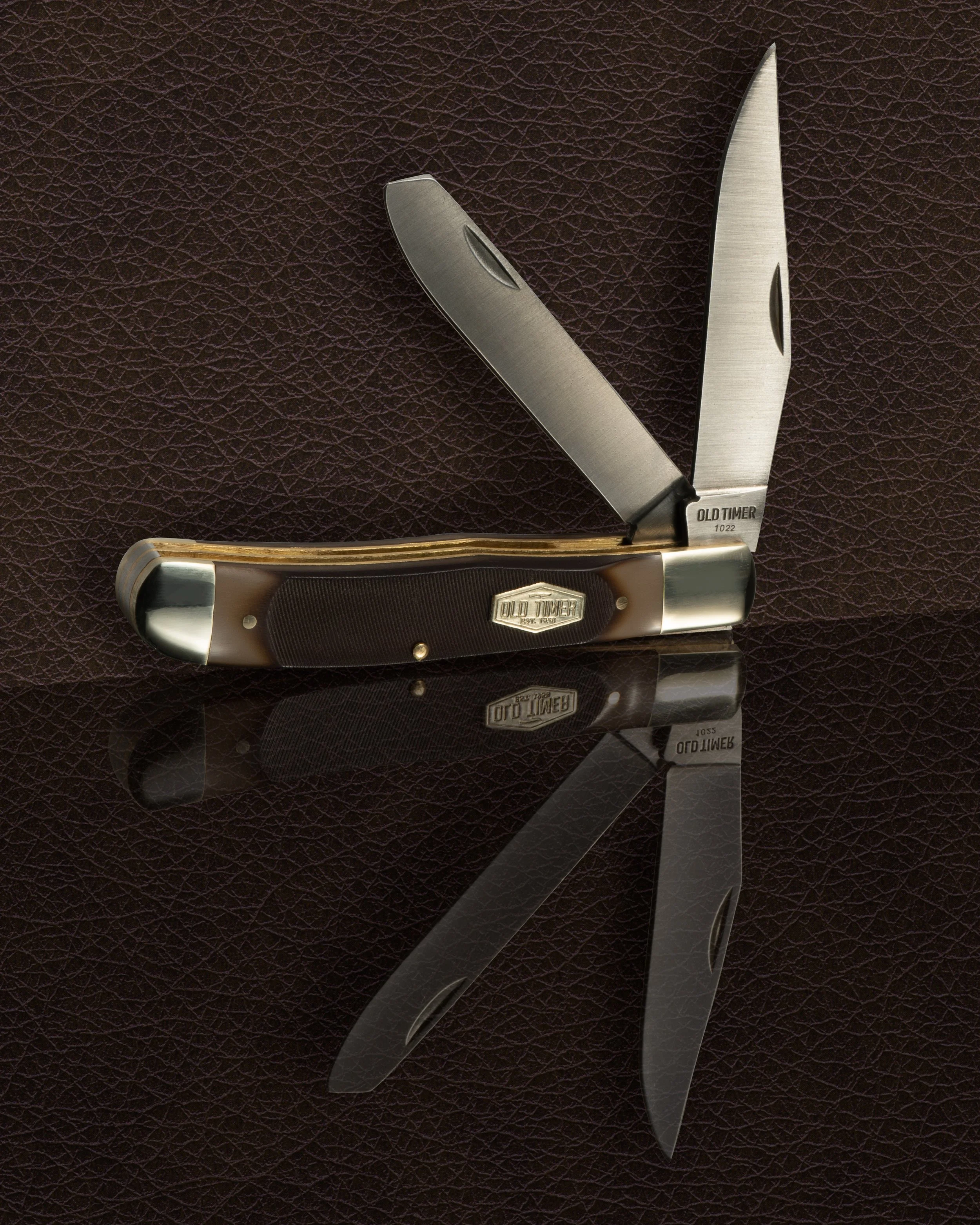 A pocket folding knife with a partially open blade, resting on a dark textured surface.