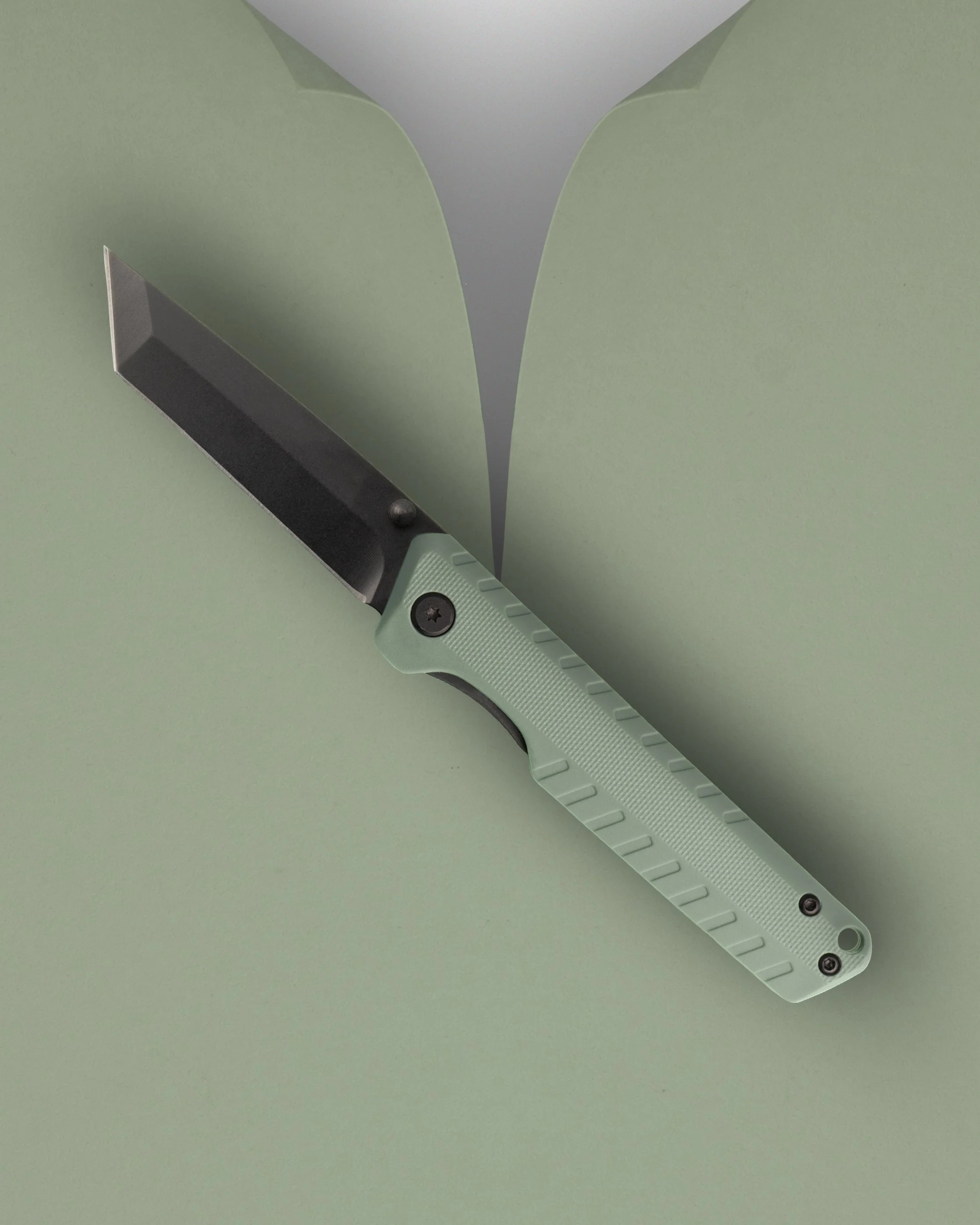 A knife with a black blade and a light green handle resting on a green surface.