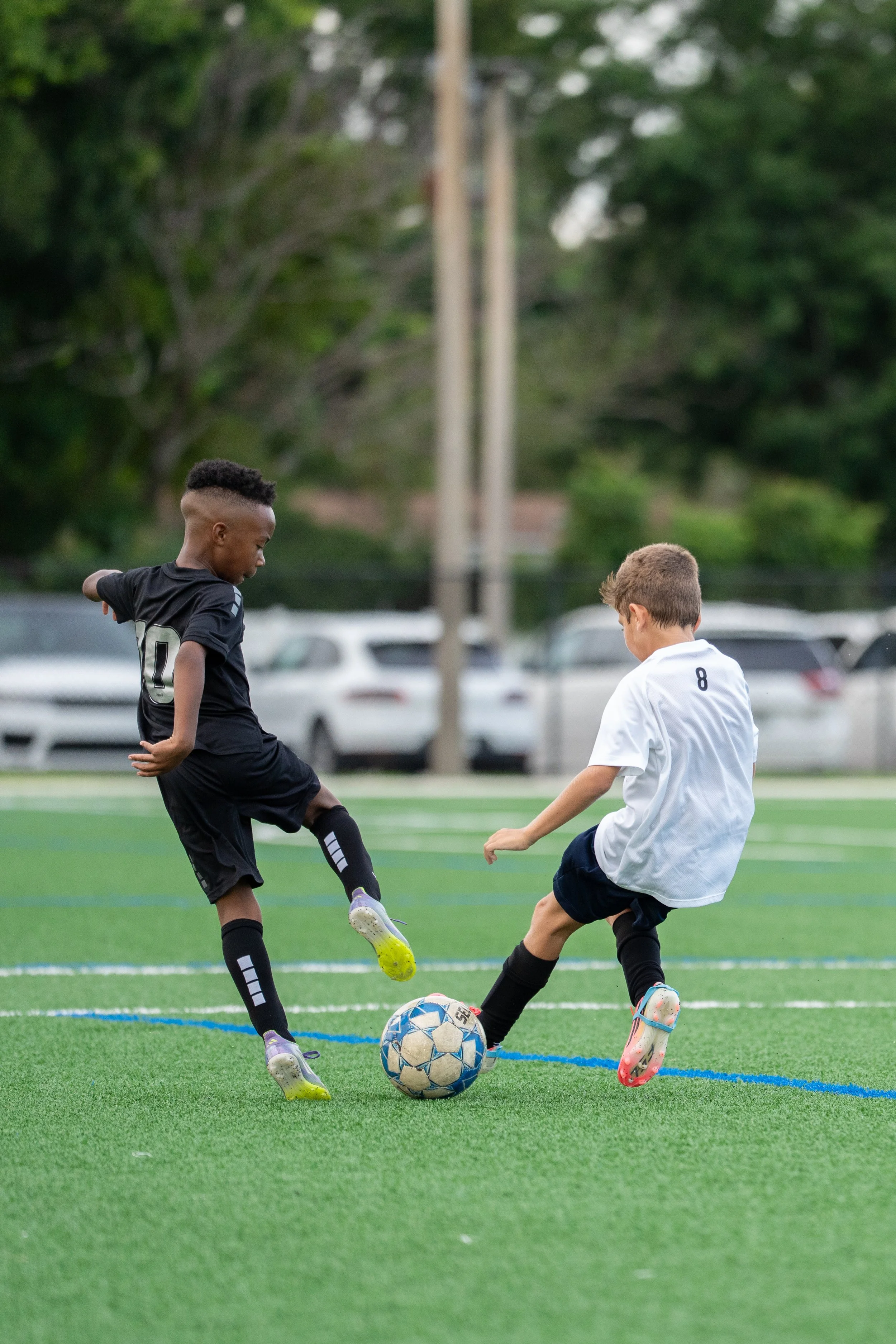 Two young boys playing soccer on a green field, kicking the ball towards each other during daytime.