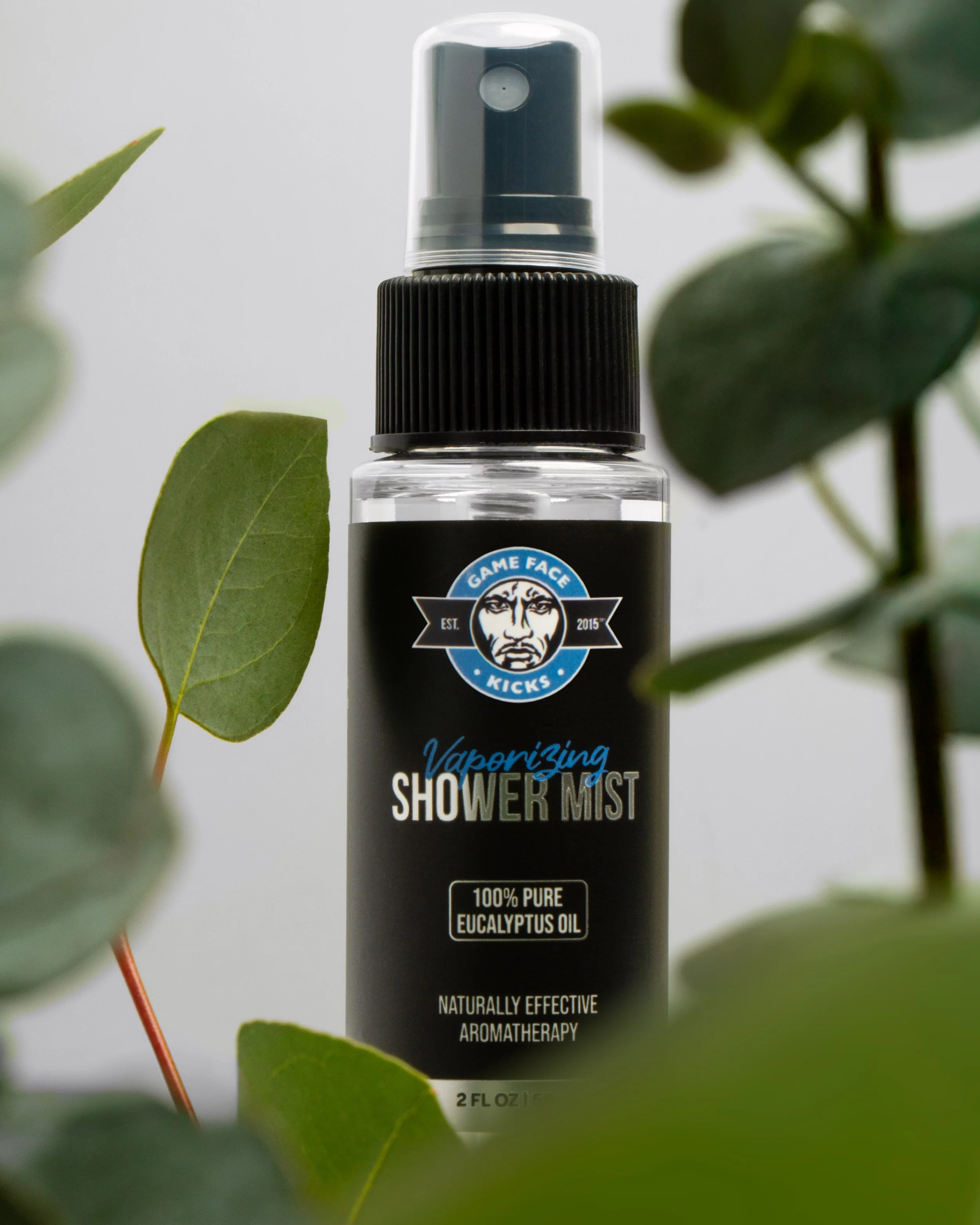 Close-up of a spray bottle labeled as vaporizing shower mist with eucalyptus oil, surrounded by green leaves.