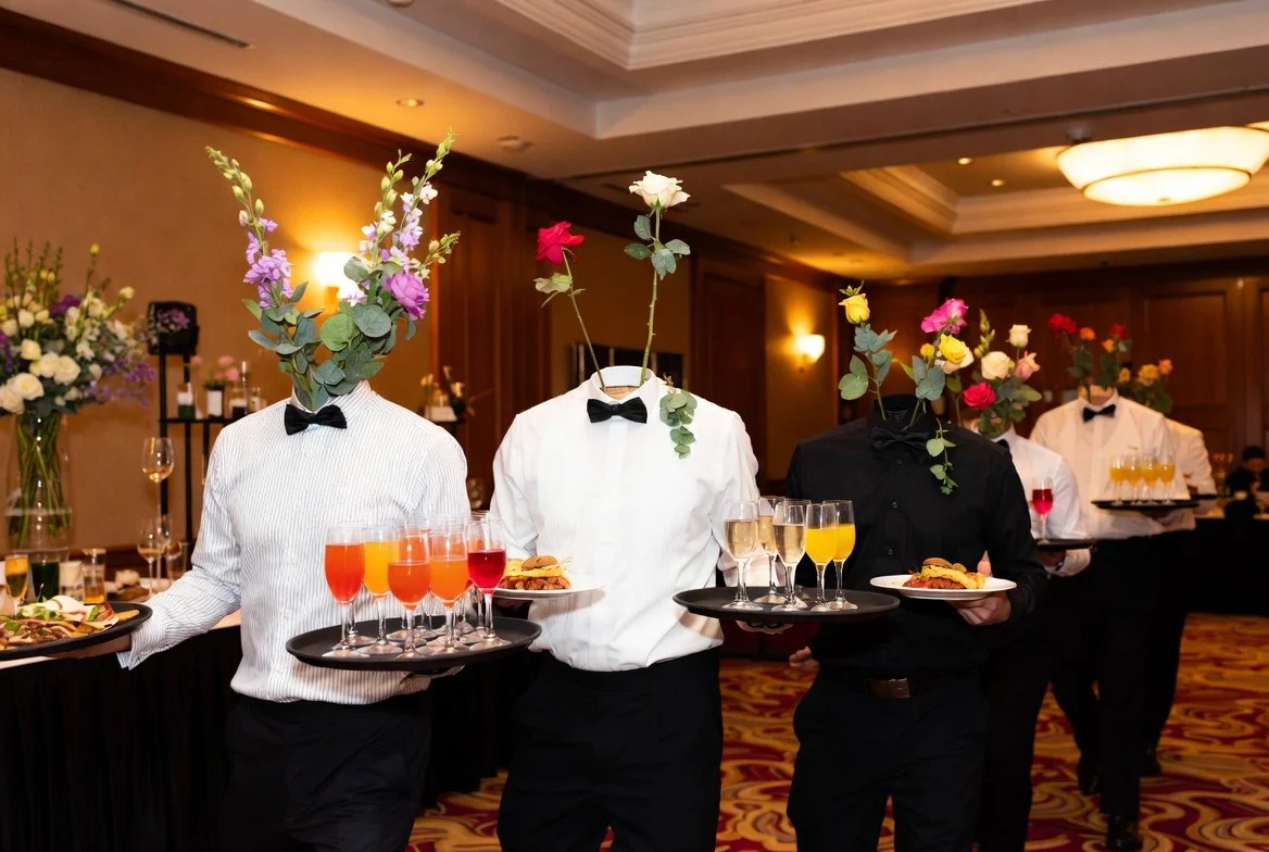 Staff serving drinks and food at a formal event in a decorated banquet hall.