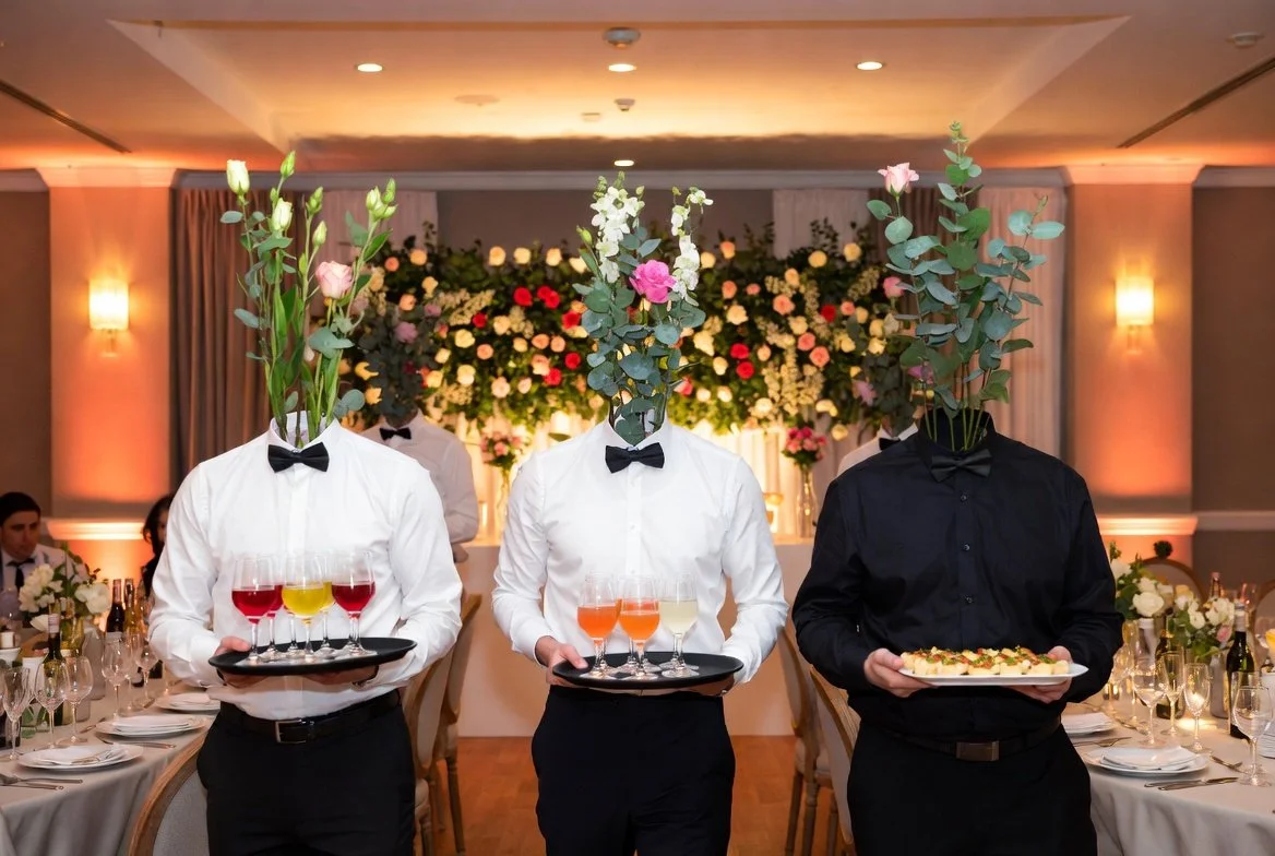 Three waiters are carrying a tray with colourful drinks or food at a decorated banquet hall for a special event or wedding.