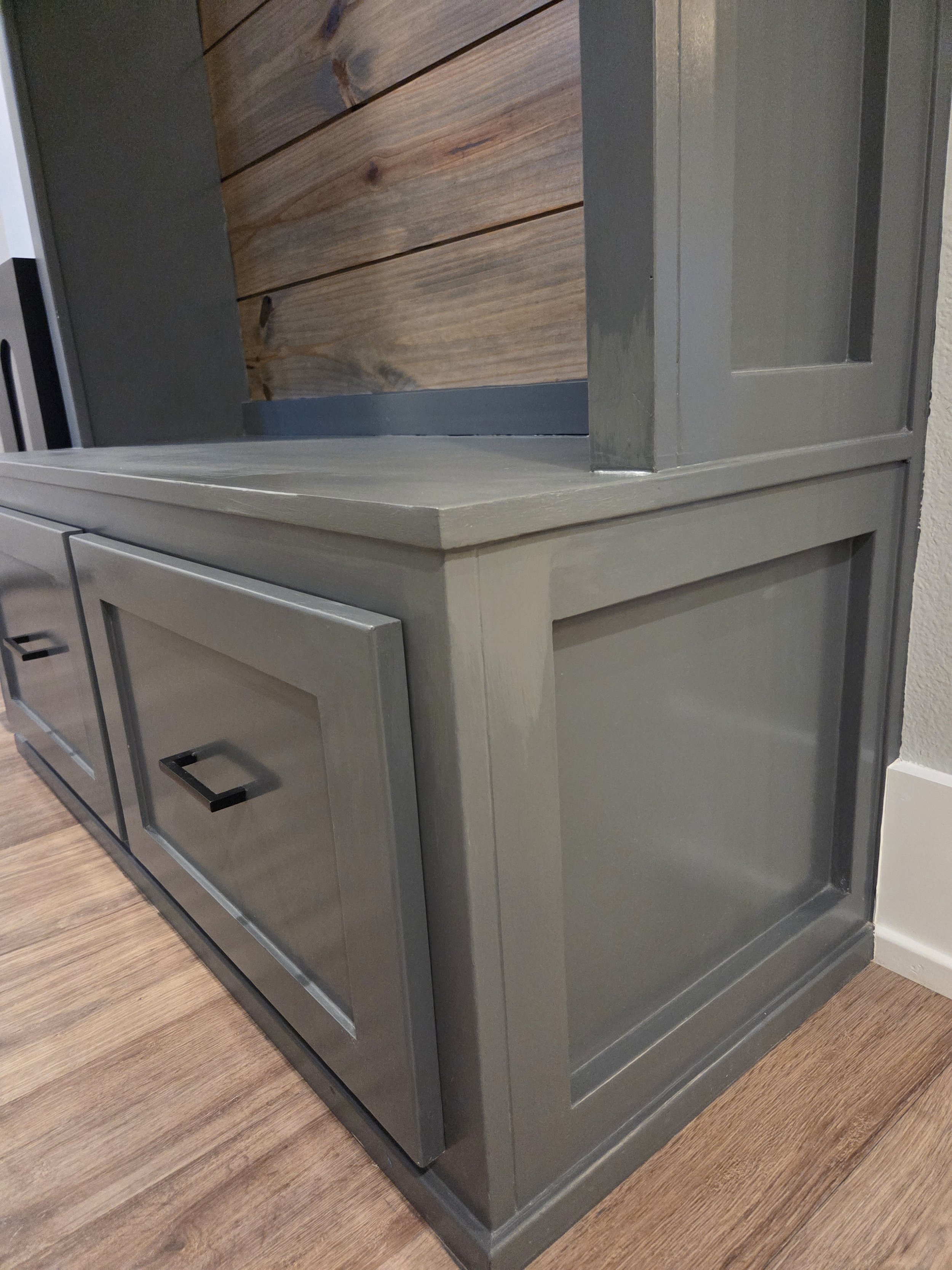 A corner of a wooden and painted gray cabinet with drawers and an open space, placed on a wood floor.