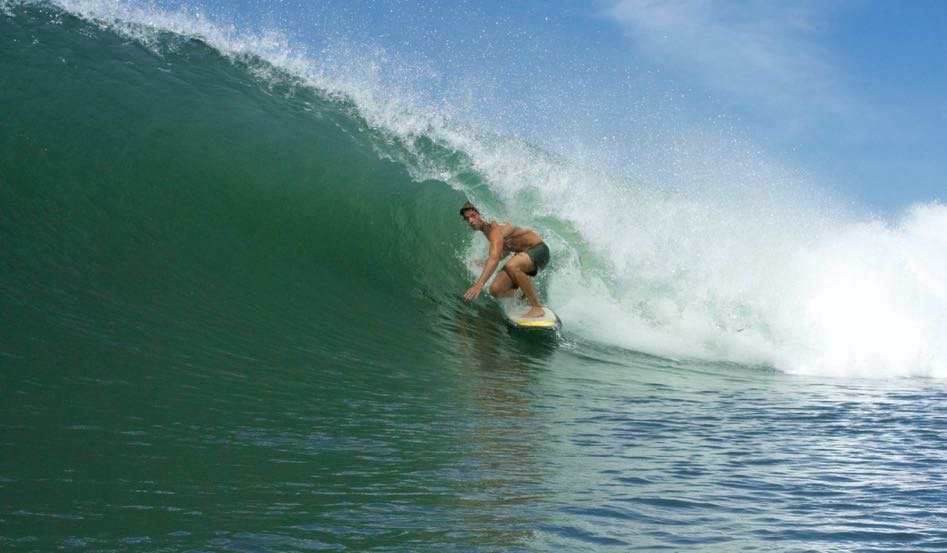 A person surfing a large green wave in the ocean under a blue sky.