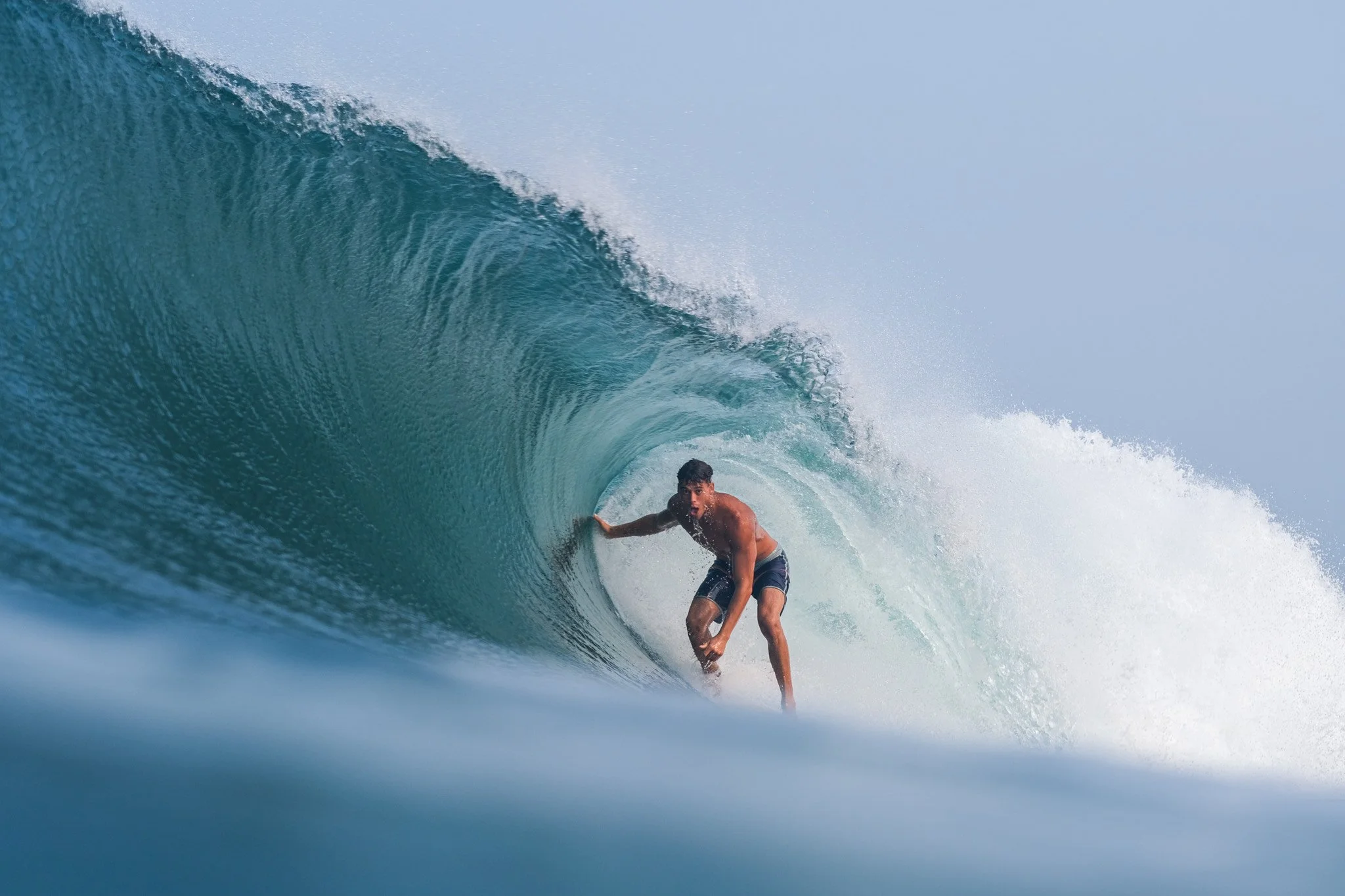 A man surfing inside a large blue wave.