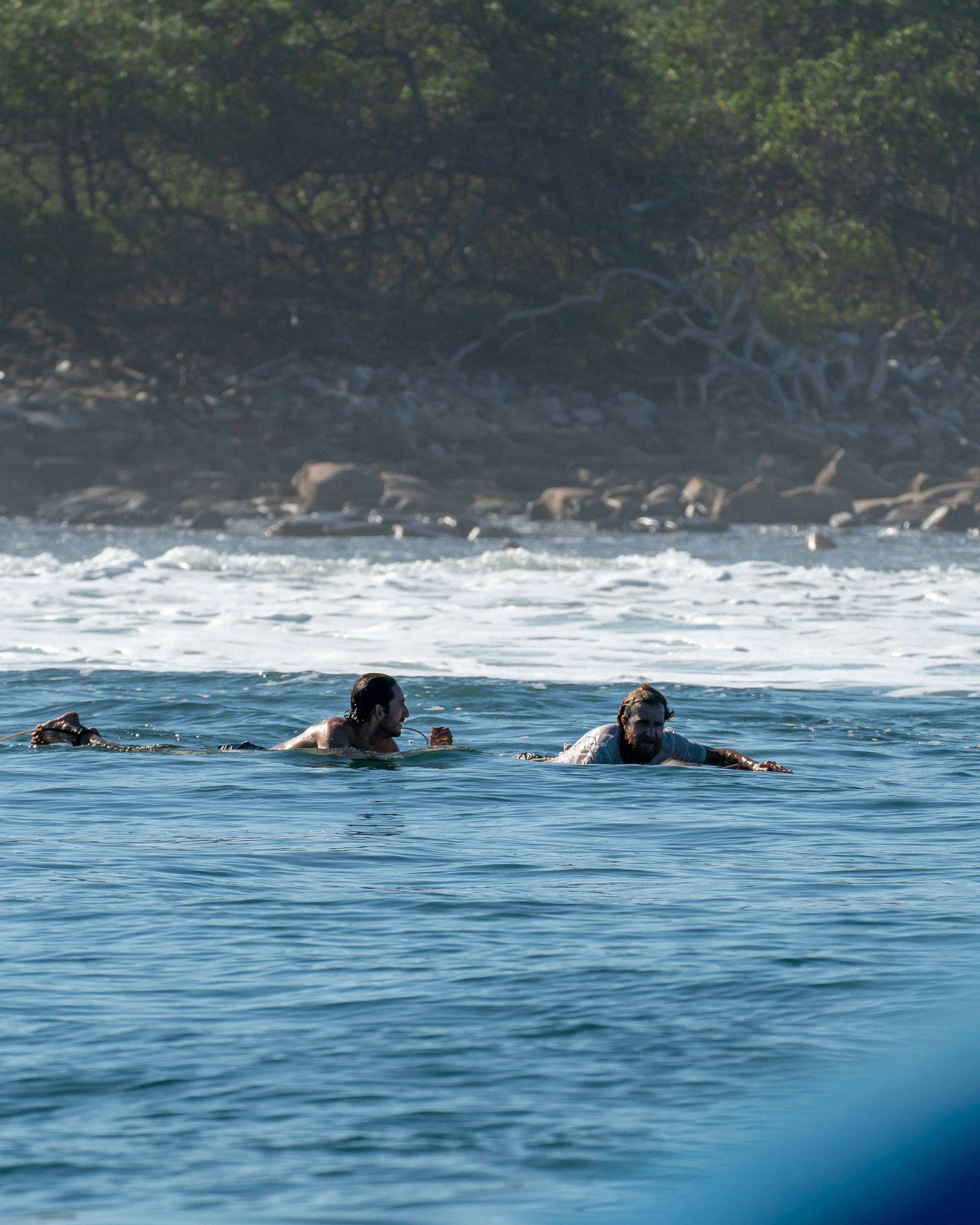 Laptop on a desk showing a surfer riding a wave at the beach with a person in curly hair in the foreground.