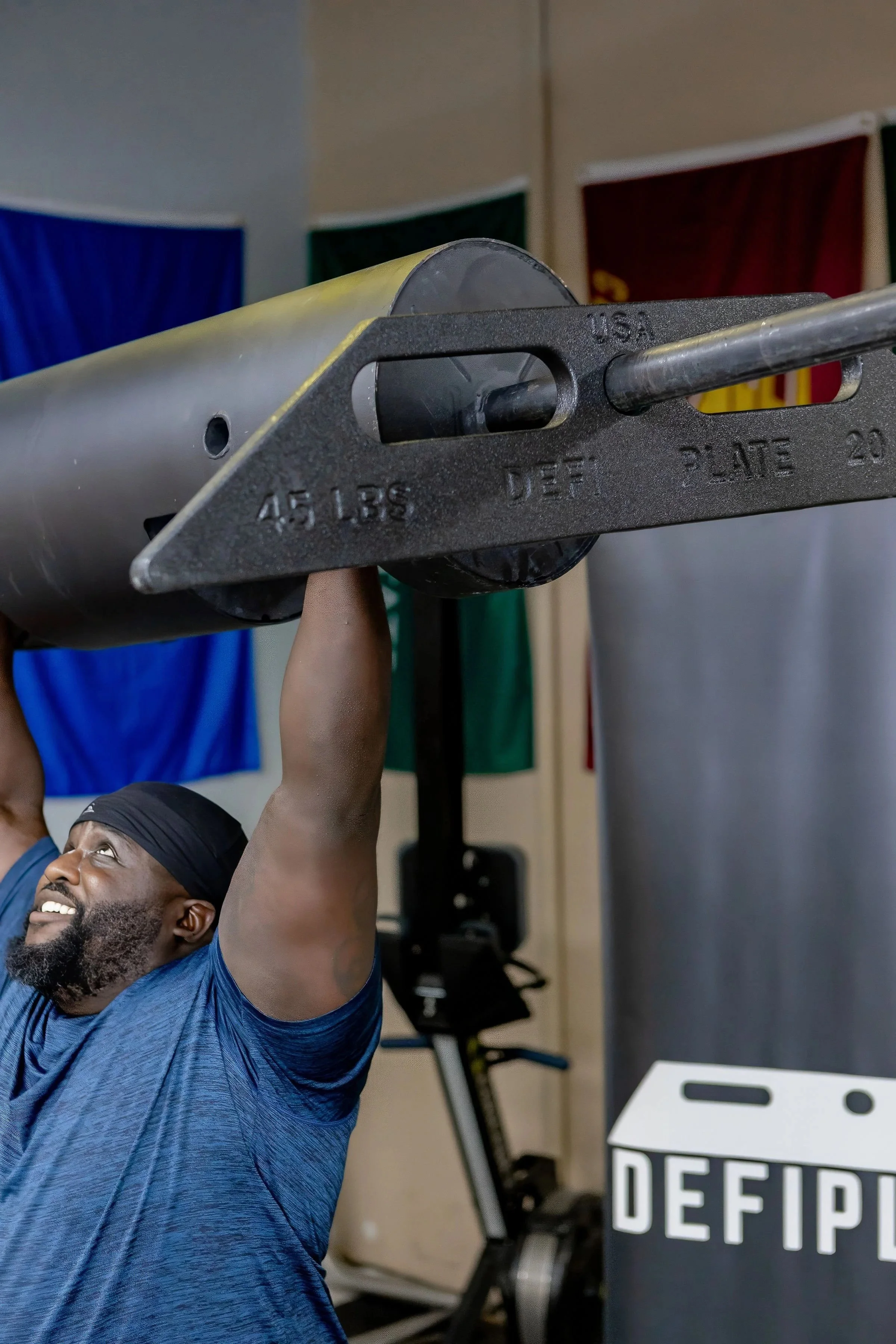 A muscular black man performs a log press with unique trapezoid weight plate that spins and rocks as he performs the exercise