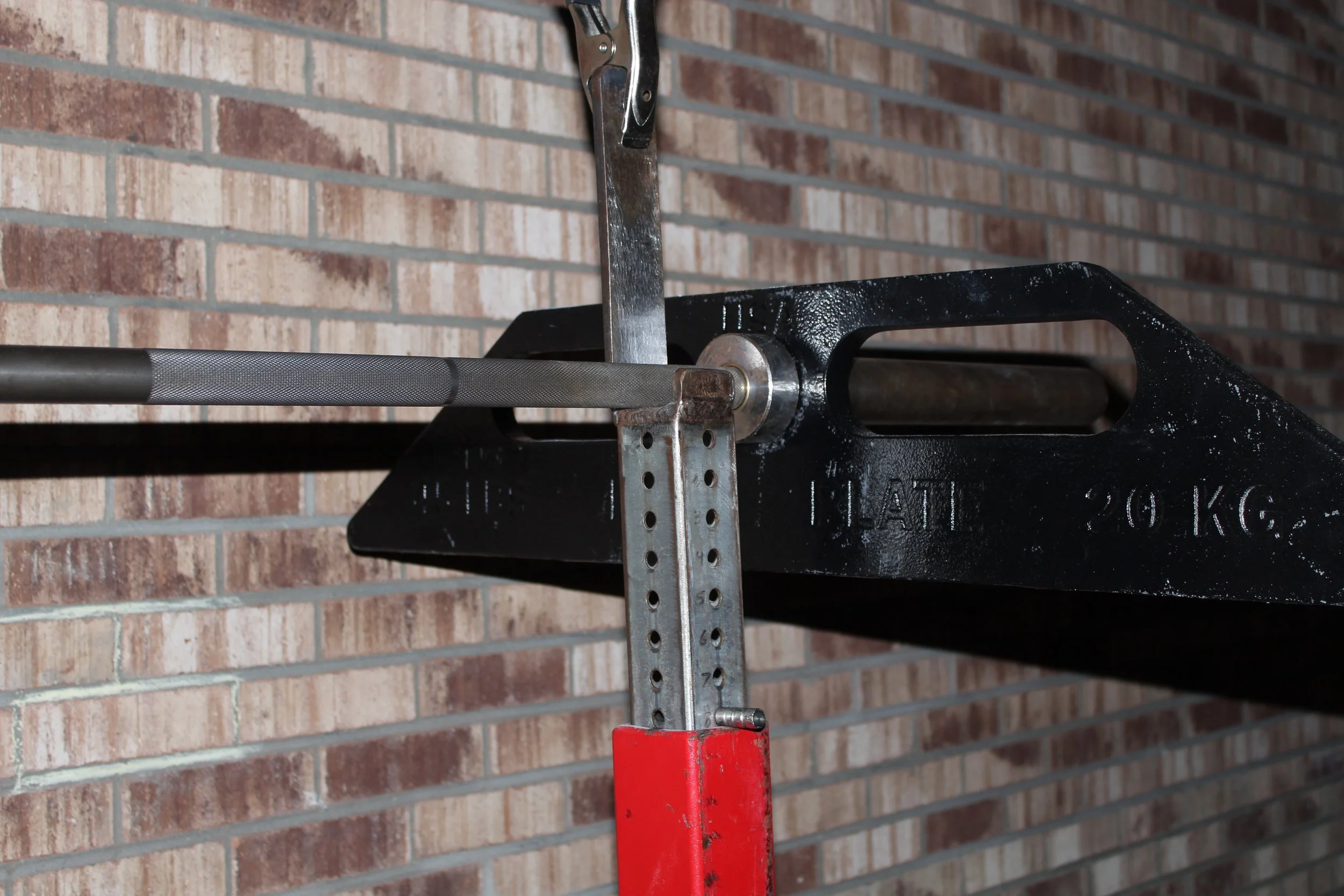 A close-up of a stability challenged barbell weight plate on a barbell stand against a brick wall.