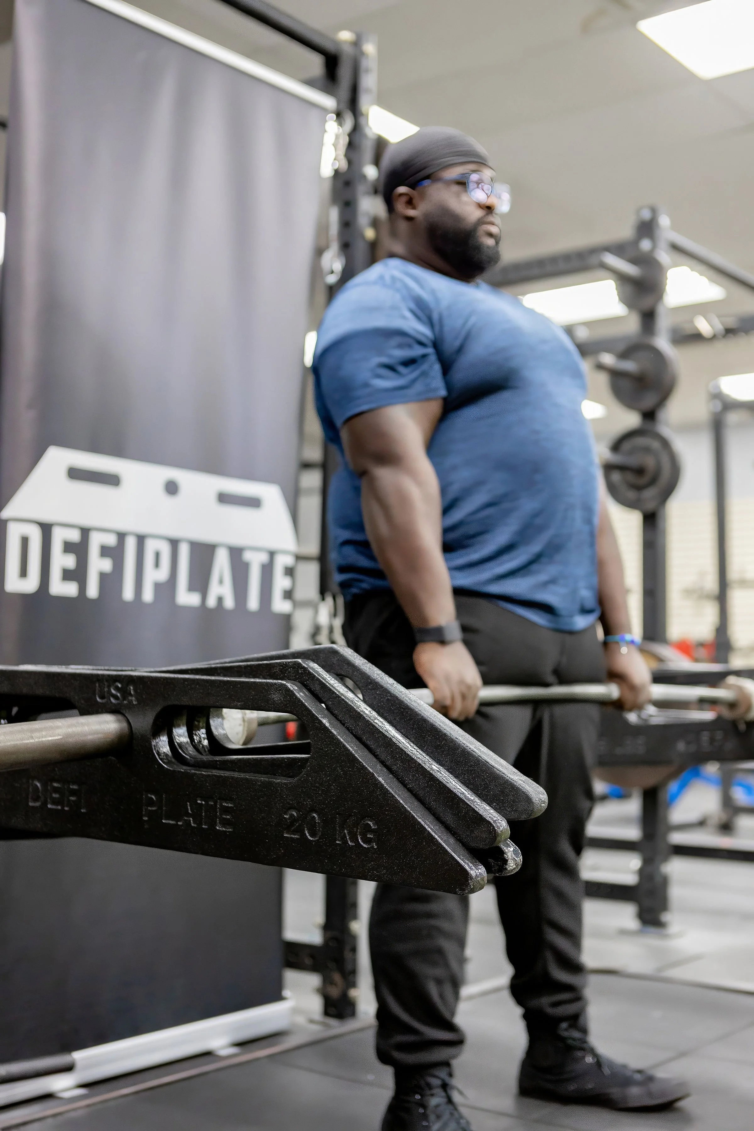 A man lifting a barbell at the gym during a deficit deadlift exercise with unique spinning trapezoid weight plates.