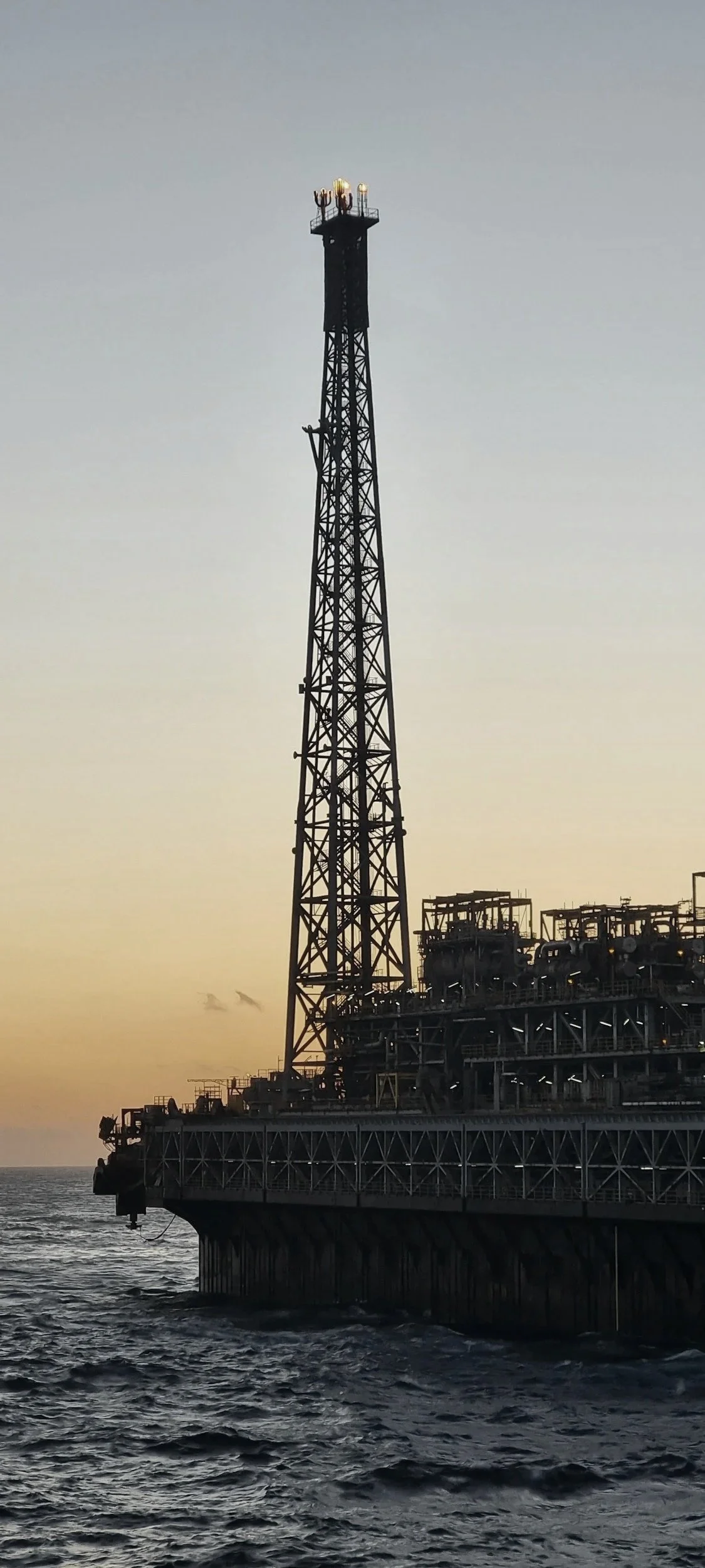 Offshore oil and gas platform with flare tower at sea during sunset, representing energy production and offshore energy infrastructure.