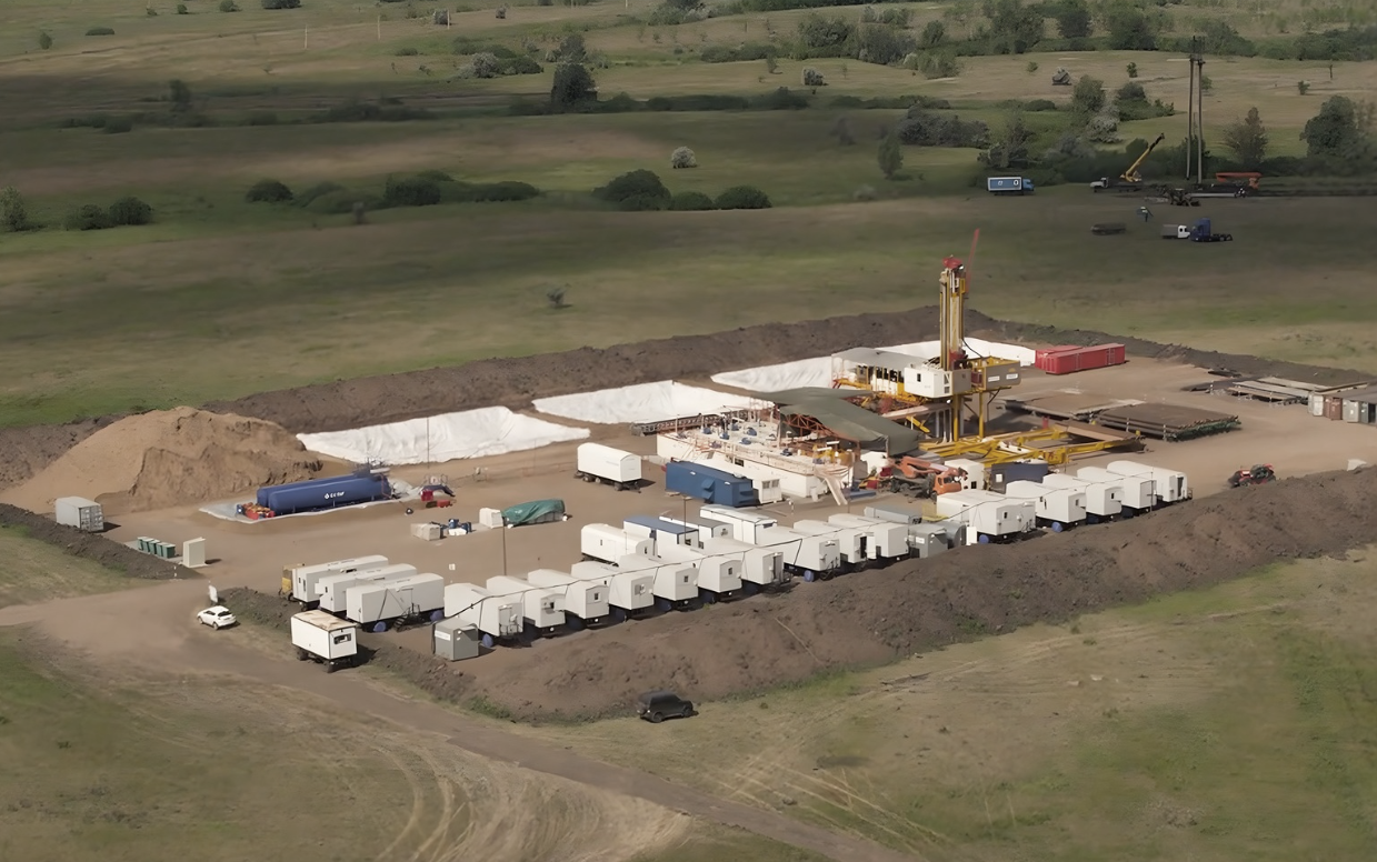 Aerial view of an onshore oil and gas drilling rig surrounded by support equipment and temporary site facilities in a rural location.