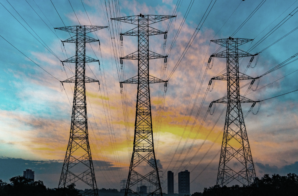 Electricity transmission towers and overhead power lines against a sunset sky, illustrating energy and utility infrastructure conflict-free risks.