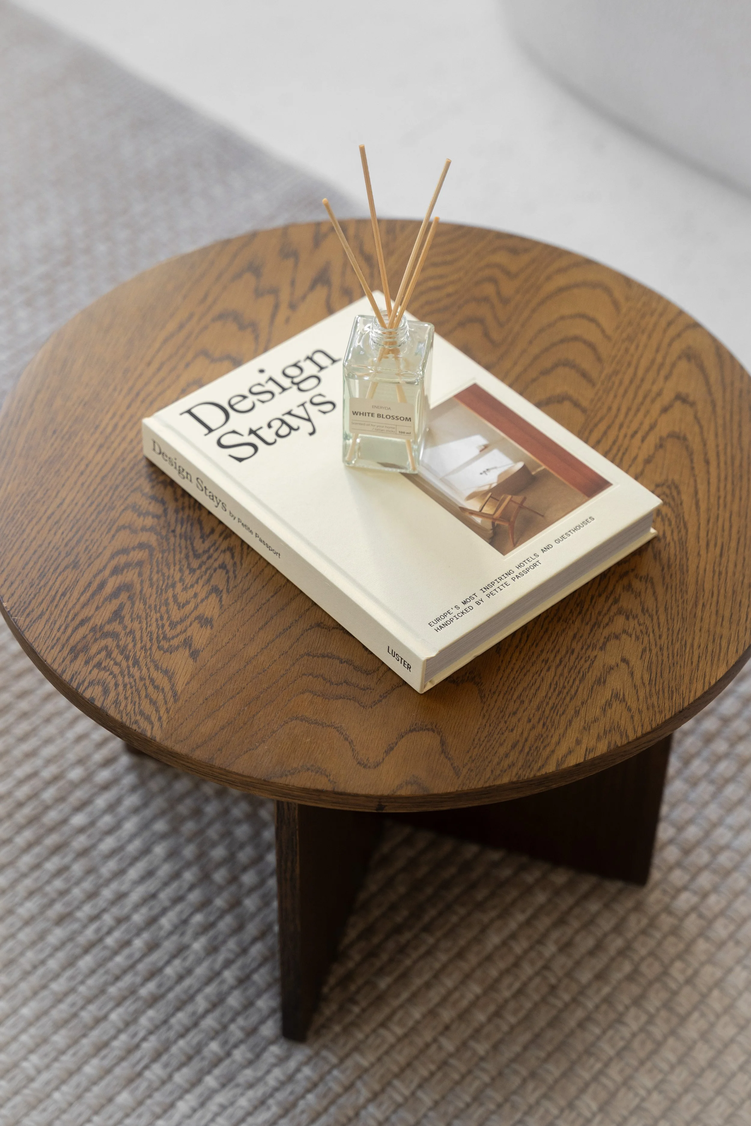 Runder Holztisch mit einem Buch und einem Raumduft-Stäbchen-Set auf der Oberfläche.