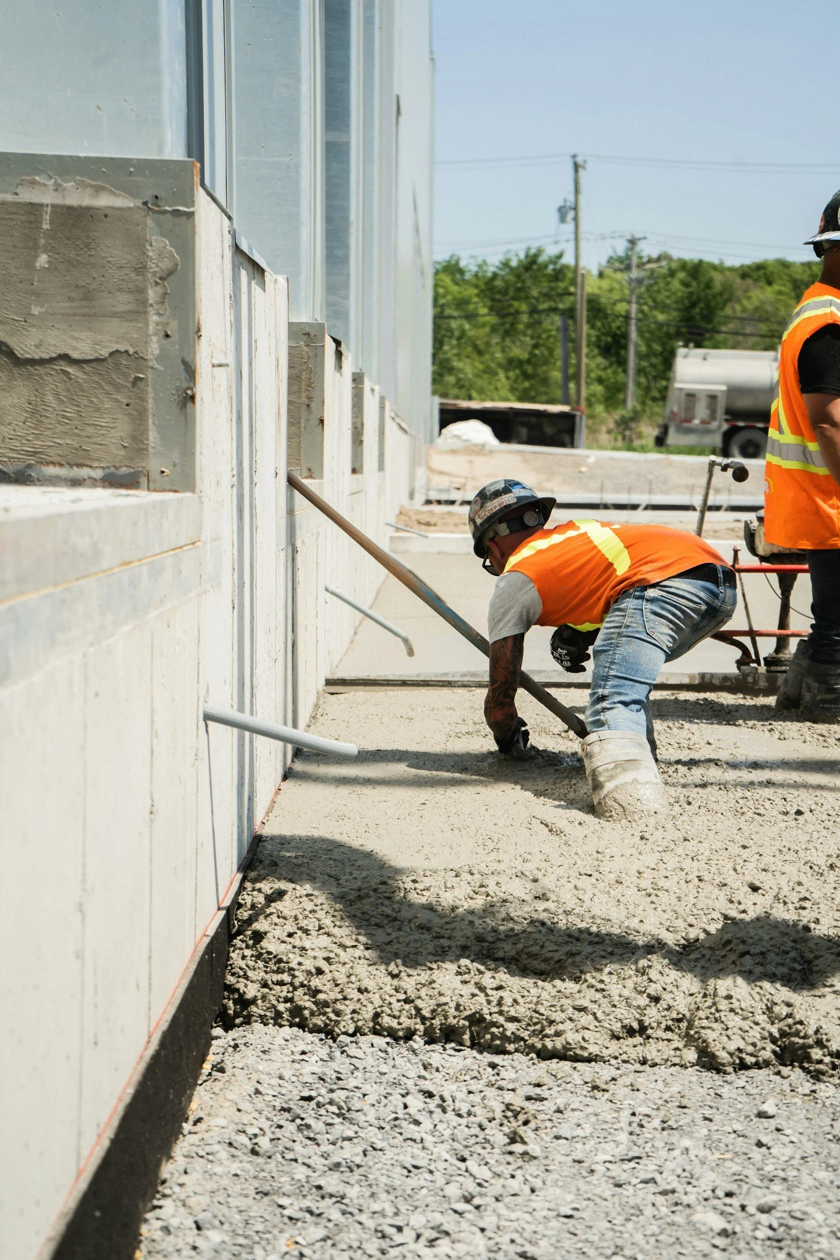 Construction workers wearing safety vests and helmets working on a concrete surface at a building site.