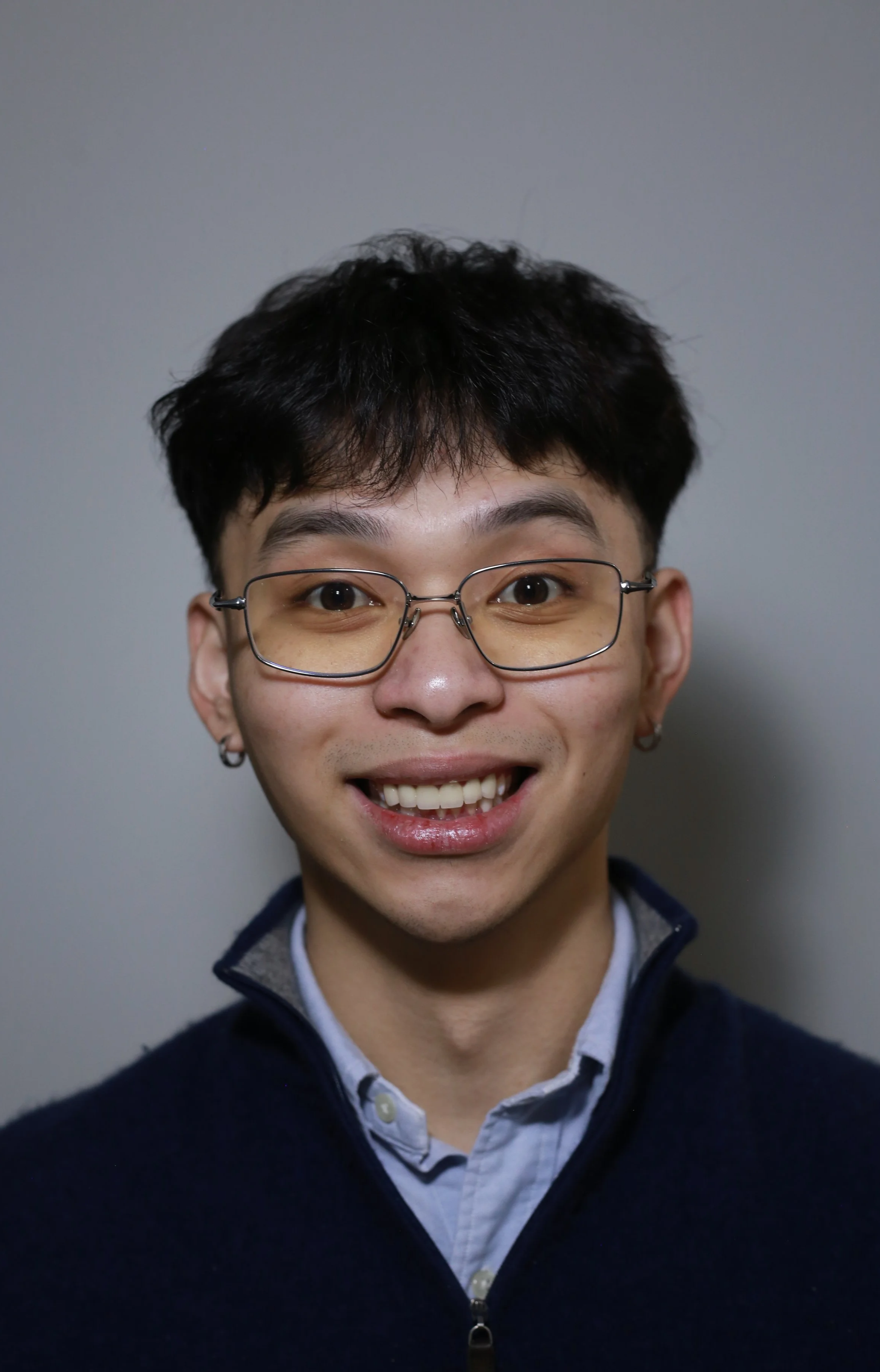 A young man with glasses smiling against a plain background.