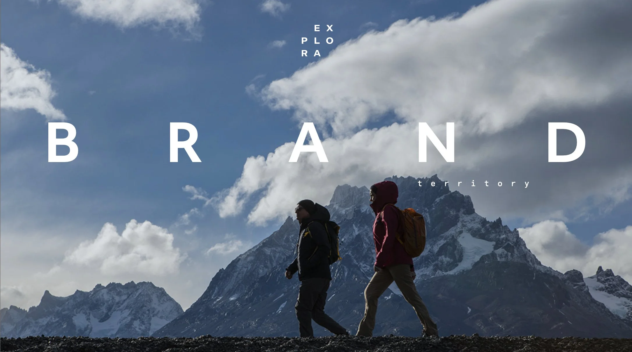 Two hikers walking in front of snow-capped mountains and a cloudy sky with the words "Explore Your Brand Territory" overlaid.