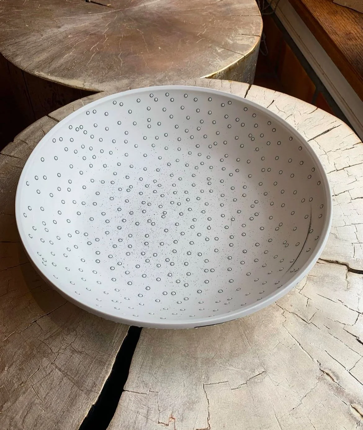 White plastic colander with small round holes, placed on a cracked wooden surface.