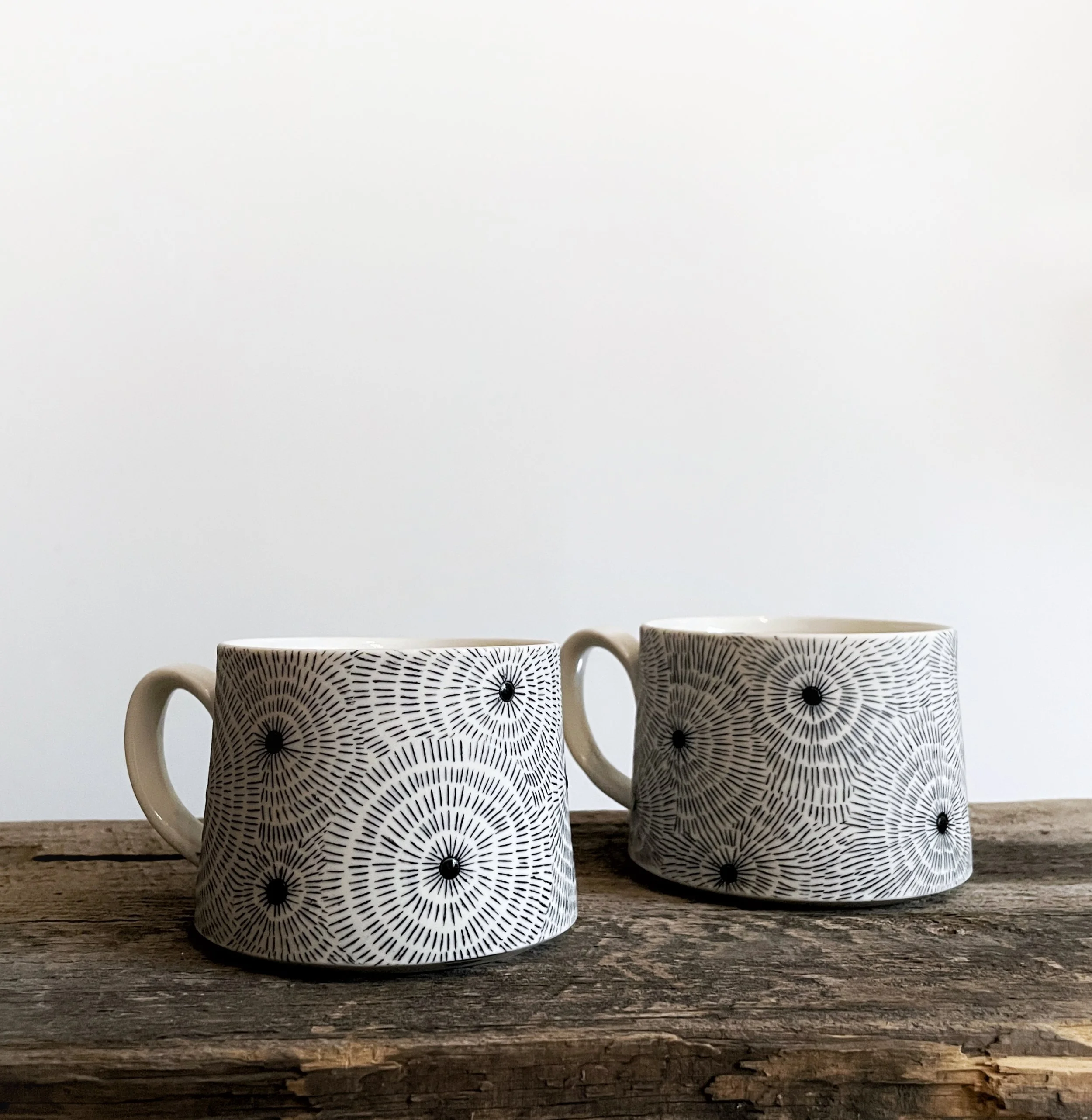 Two ceramic mugs with black and white geometric spiral patterns on a wooden surface against a plain white background.