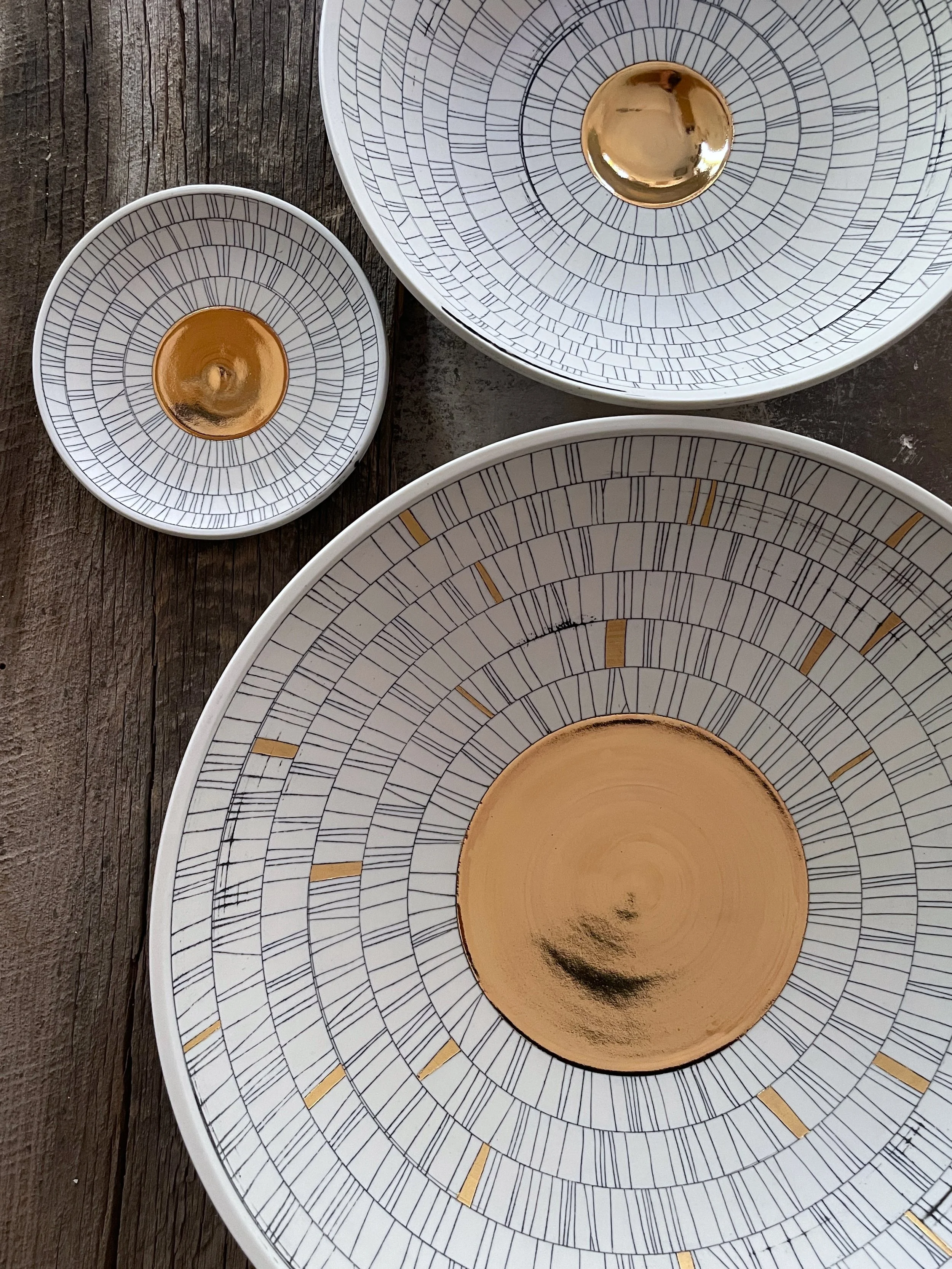 Set of four white plates with black and gold geometric patterns and gold centers, placed on a rustic wooden surface.