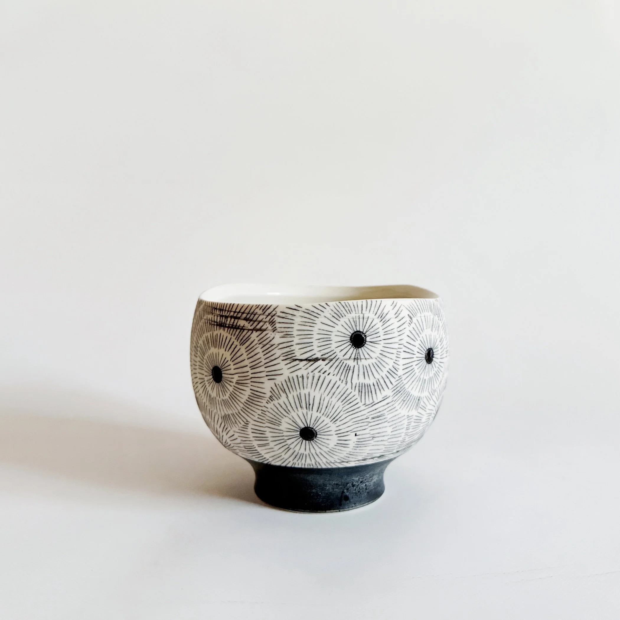 Ceramic bowl with black and white radial pattern and black dots, set against a plain white background.