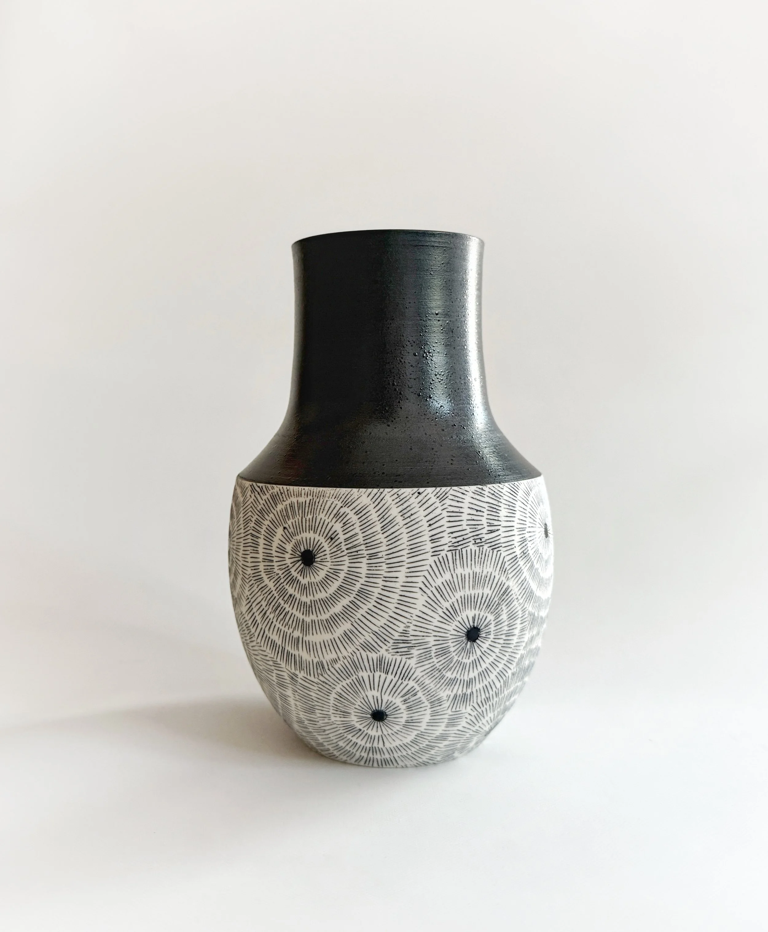 Black and white ceramic vase with geometric circular patterns on the lower part and a plain black upper part, set against a plain white background.