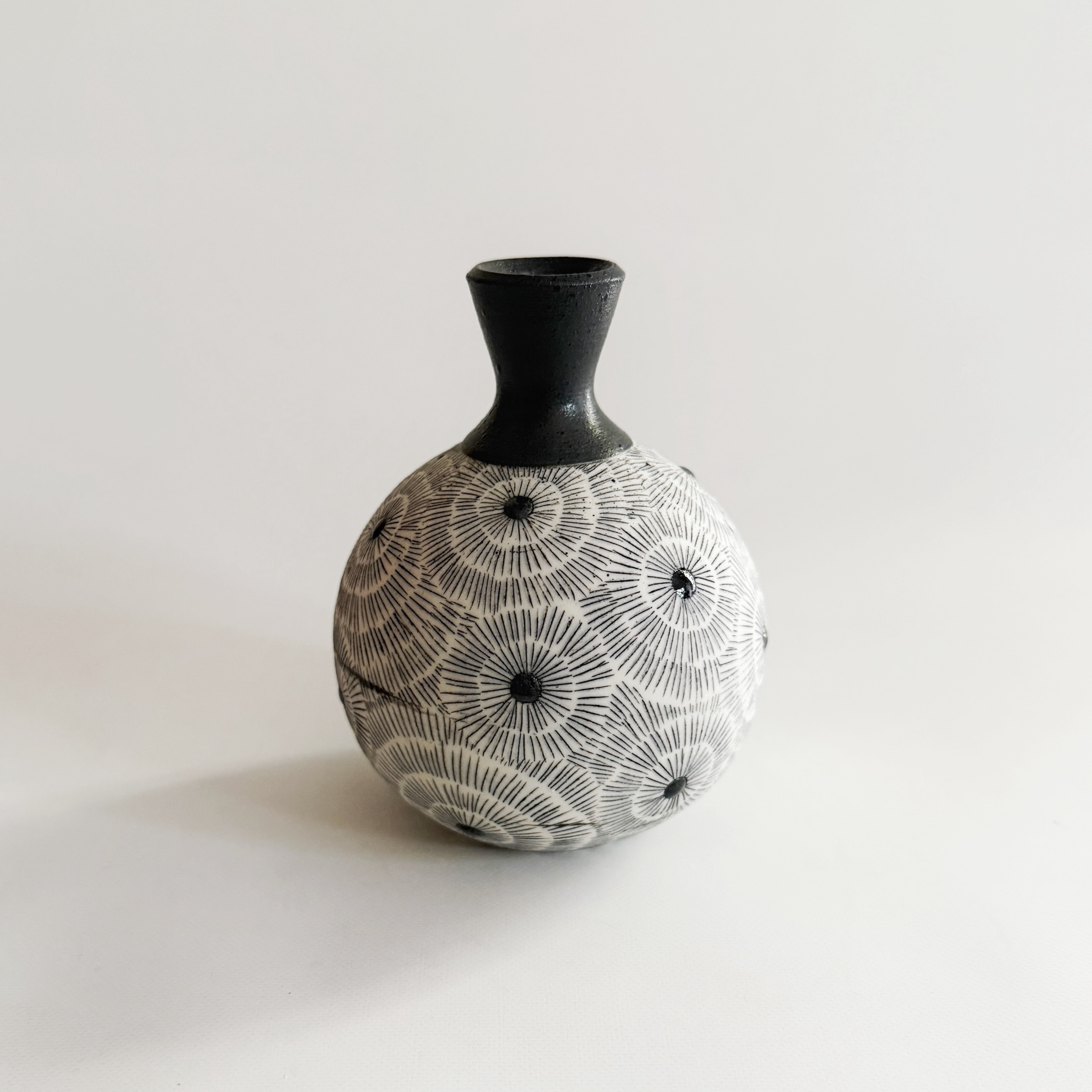 Decorative black and white ceramic vase with geometric and radiating line patterns, set against a plain white background.