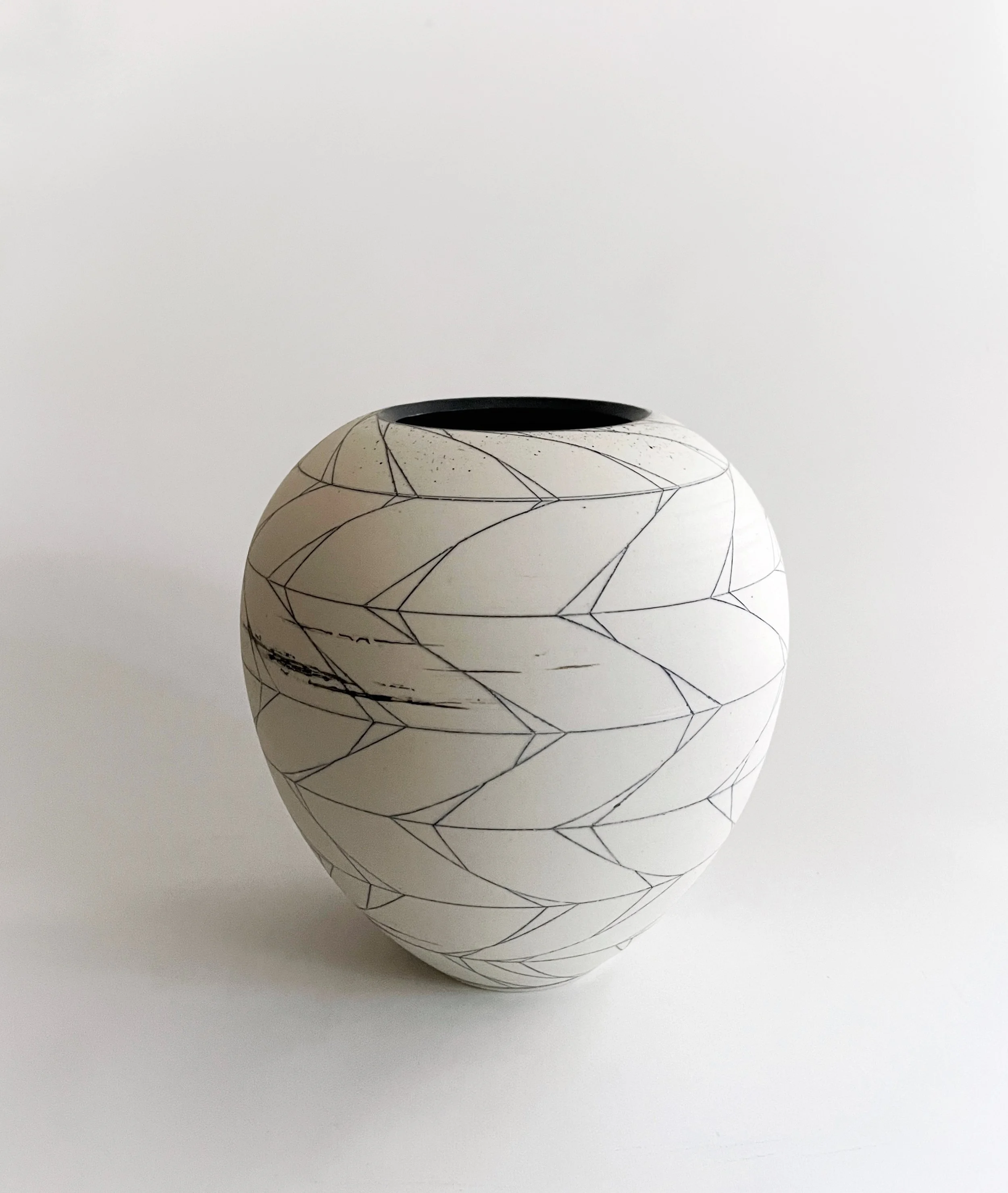 White ceramic vase with black geometric line patterns on a plain white background.