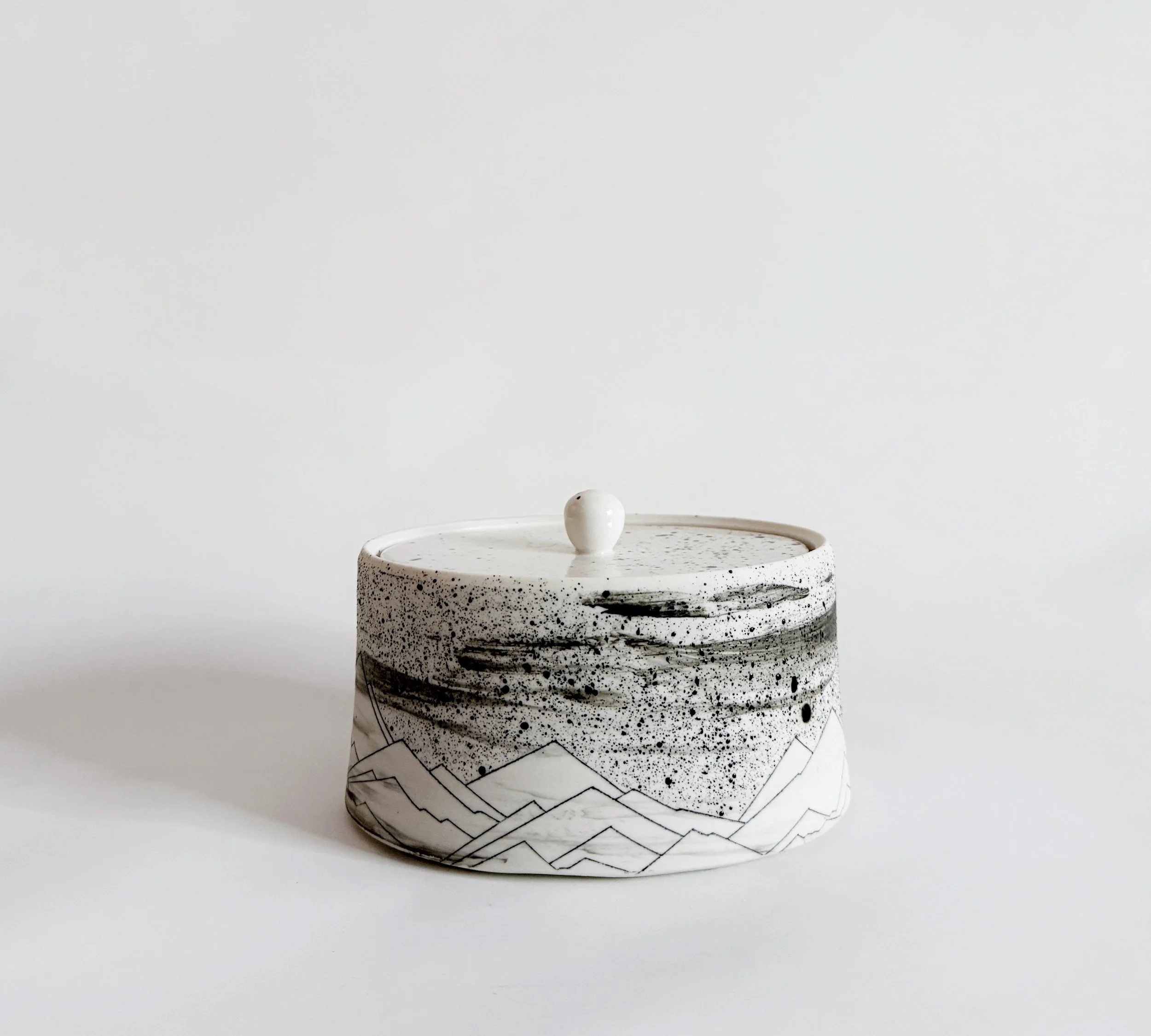 Ceramic container with a mountain landscape design on a white background.
