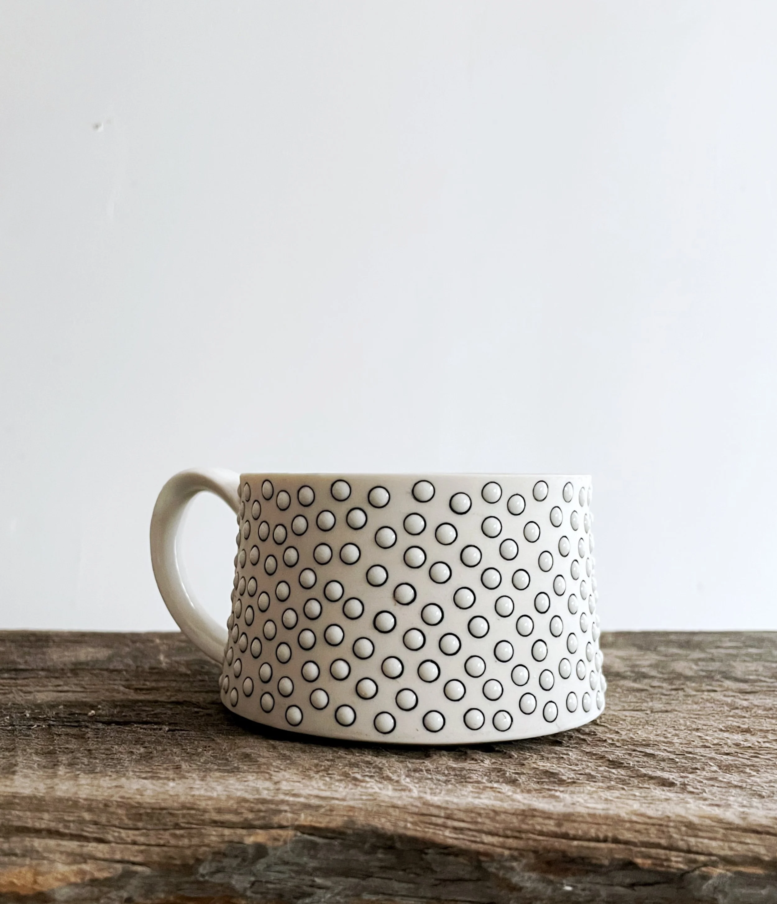 White mug with black circular dots pattern on a wooden surface against a plain white background.