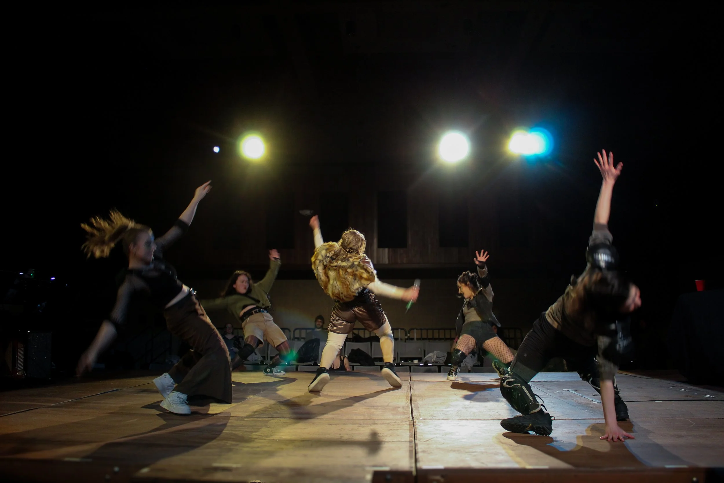 Group of five people dancing on a stage with colorful lights overhead.