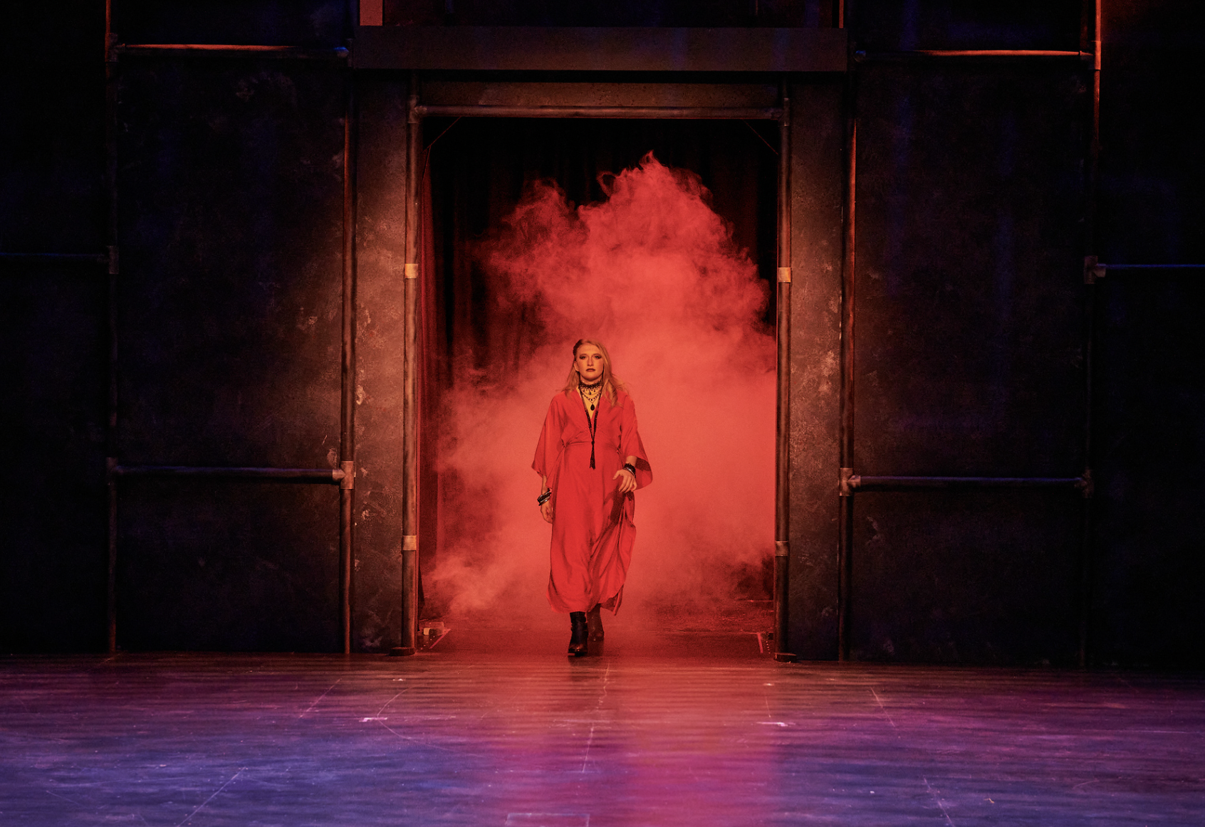 A woman in a red dress walking through a smoky stage doorway with red lighting.