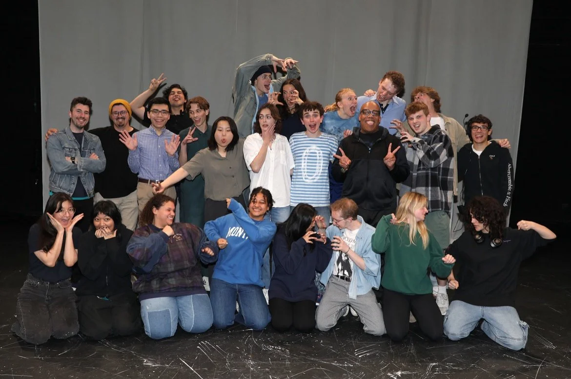 Group photo of 20 young adults on a stage making various playful and expressive gestures, celebrating together.