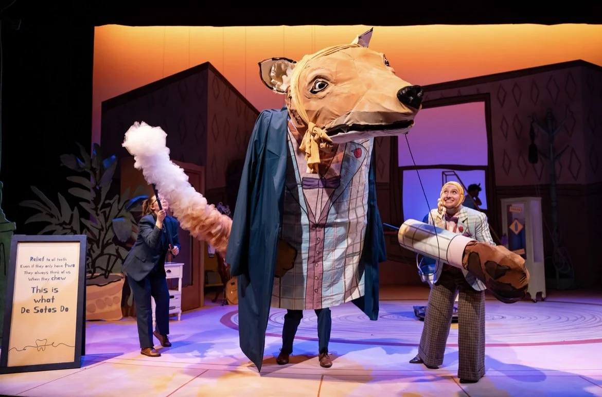 A theatrical stage with a large puppetry of a dog dressed like a detective, holding a large cigar. Two actors in suits are interacting with the puppet, one holding a feather duster and the other holding a large cigar prop. There is a signboard on the side that says “Relief to all teeth...” and a colorful backdrop.