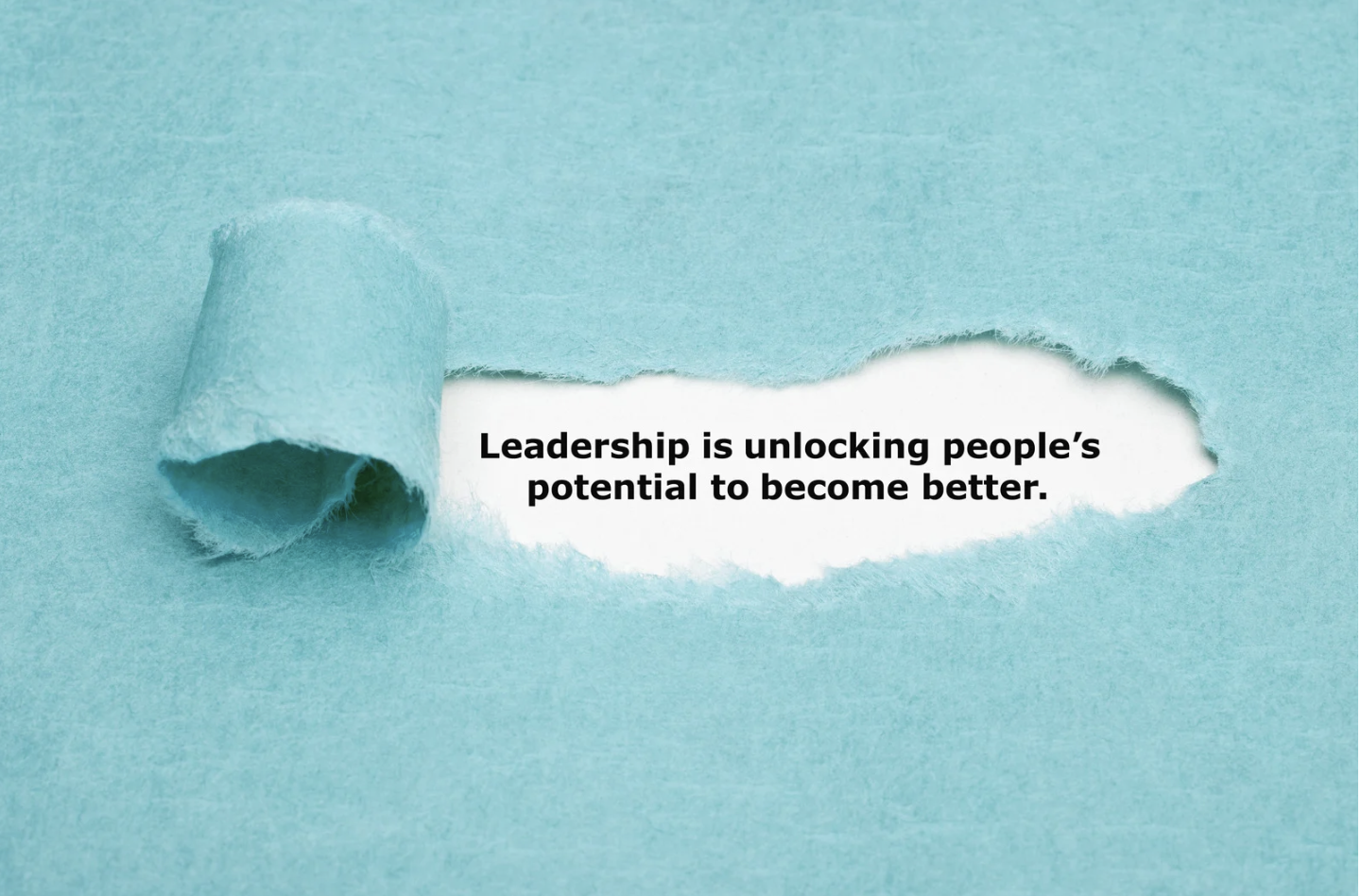 A piece of light blue torn paper revealing a quote that reads: 'Leadership is unlocking people's potential to become better.'
