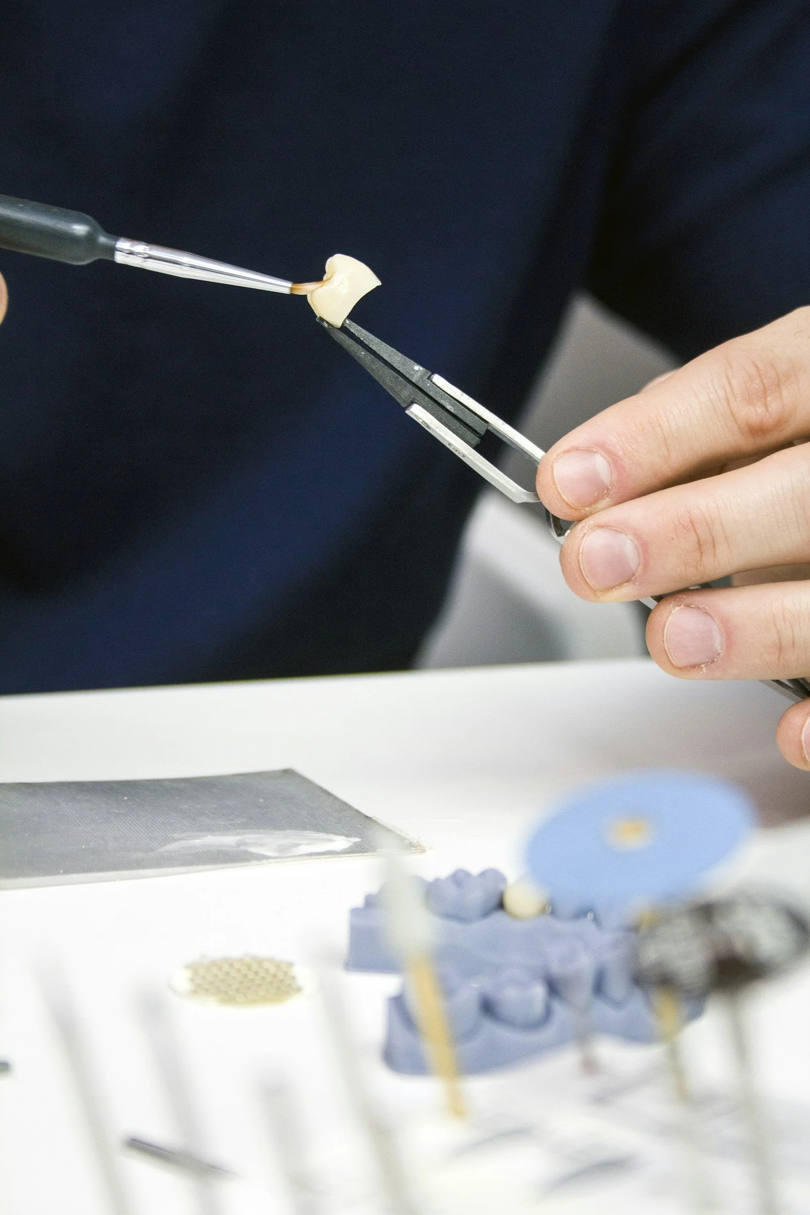 A dental technician working on a dental prosthetic or dental mold using precision tools in a lab setting.