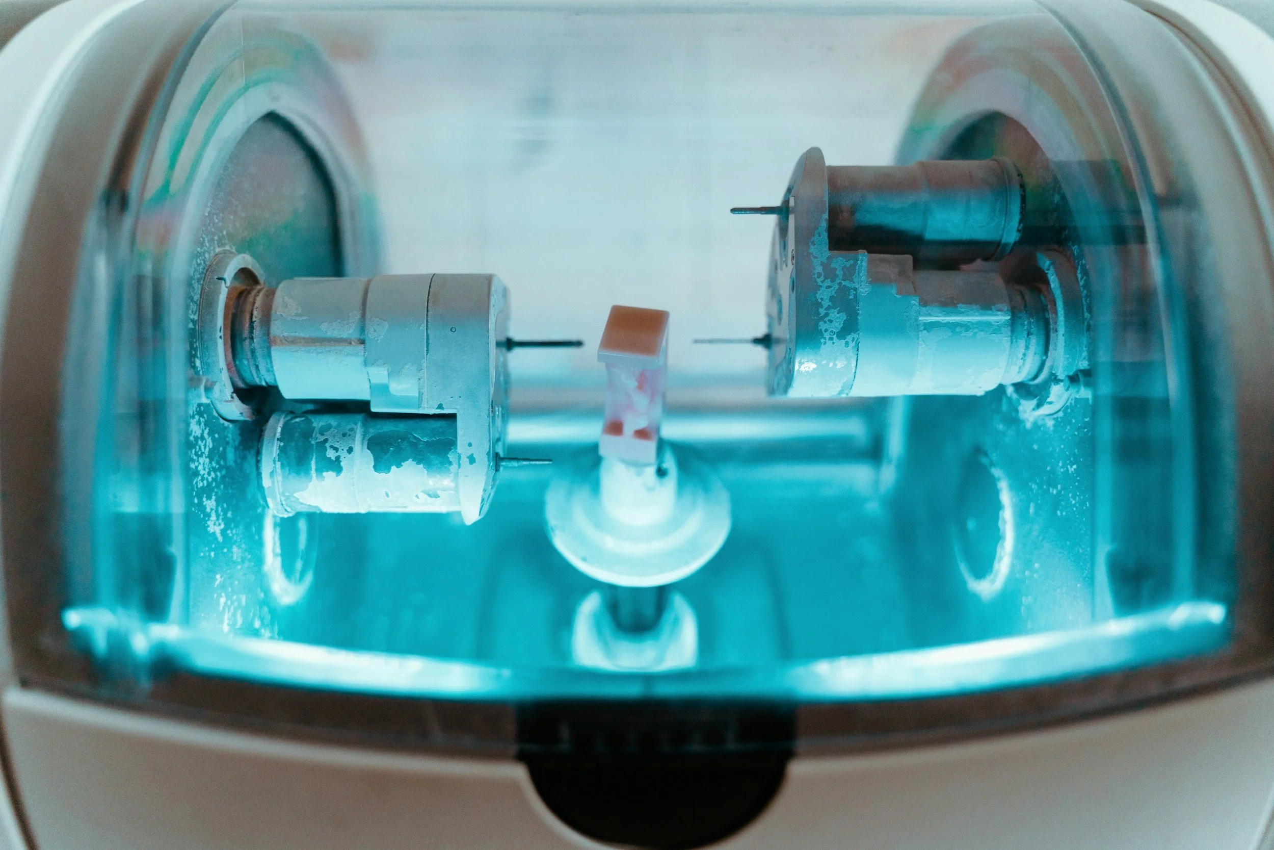 Close-up of a laboratory machine with two cylindrical components and a central digital display, inside a transparent enclosure.