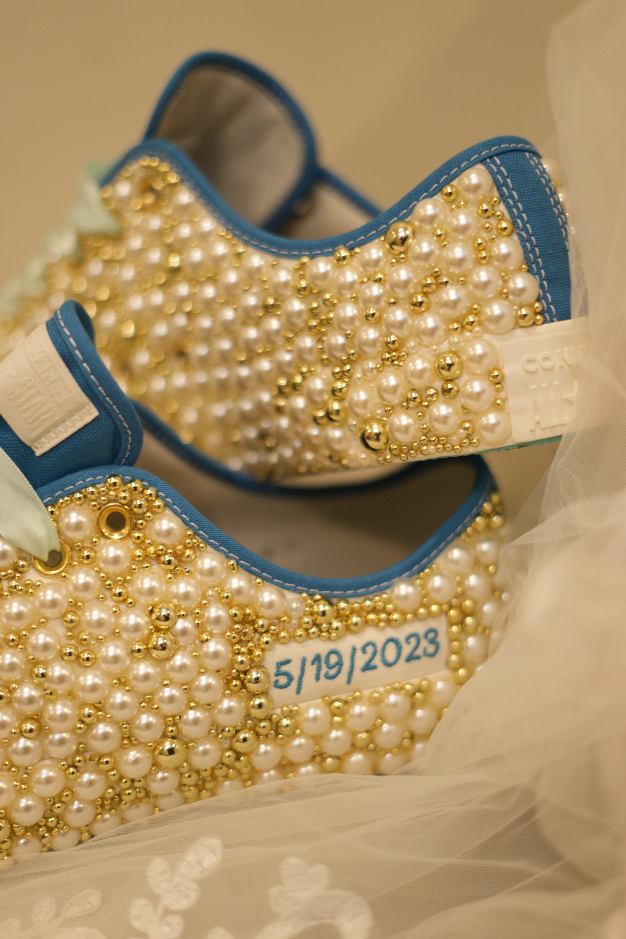 A pair of decorated sneakers covered with pearls and gold beads, with a date '5/19/2023' written on one shoe.