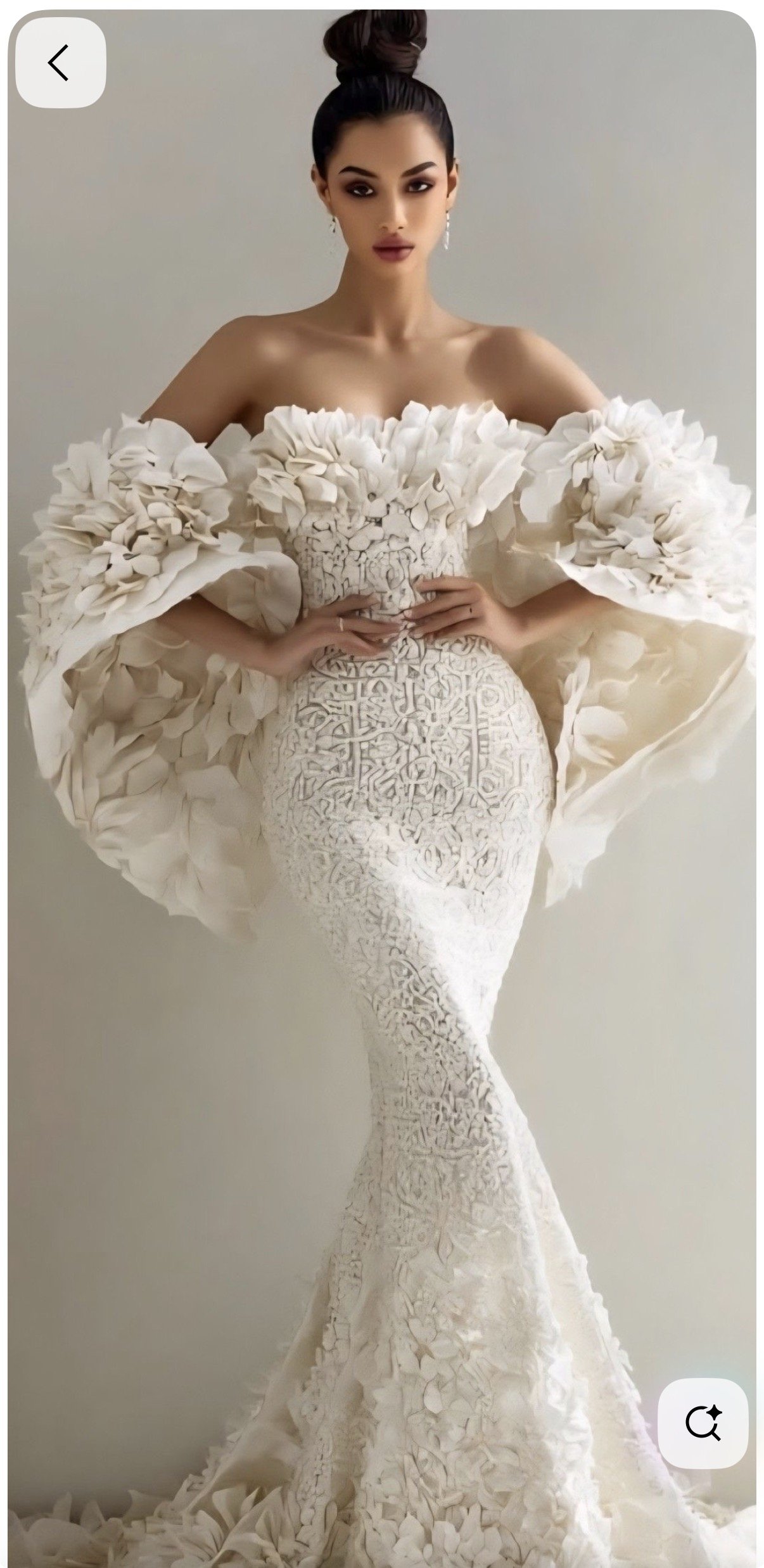 A woman in an elaborate, off-the-shoulder, cream-colored gown with textured floral and lace details. Her dark hair is styled in an elegant updo, and she has makeup with dark lipstick. She is standing against a plain, light background.