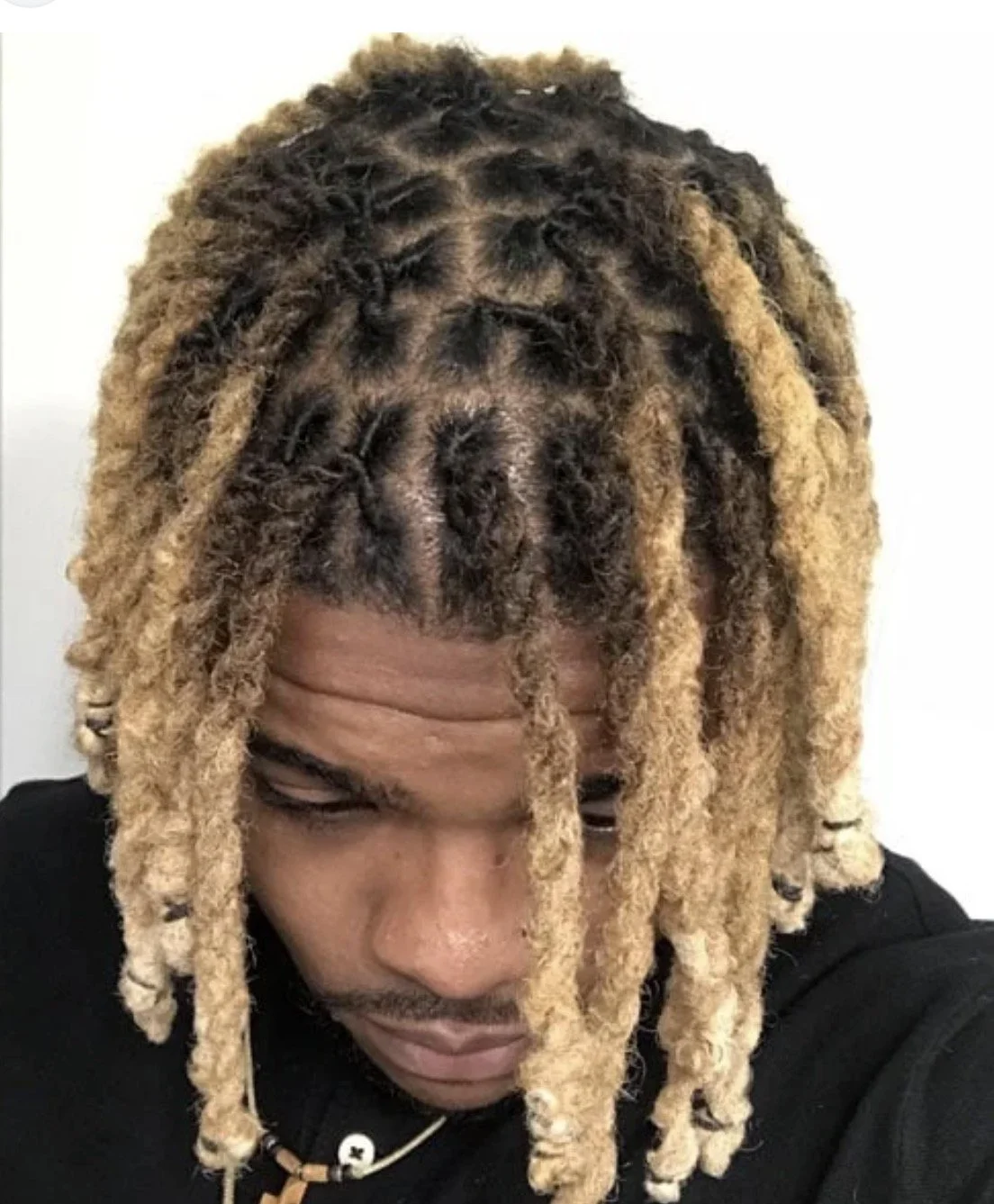 A person with blonde dreadlocks looking down, with their head tilted forward.