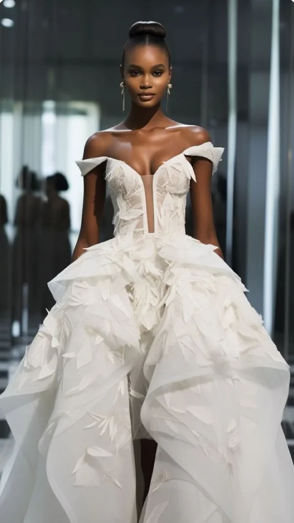 A woman wearing an elaborate white wedding dress with feather-like details and off-shoulder style, standing indoors in front of mirrors.