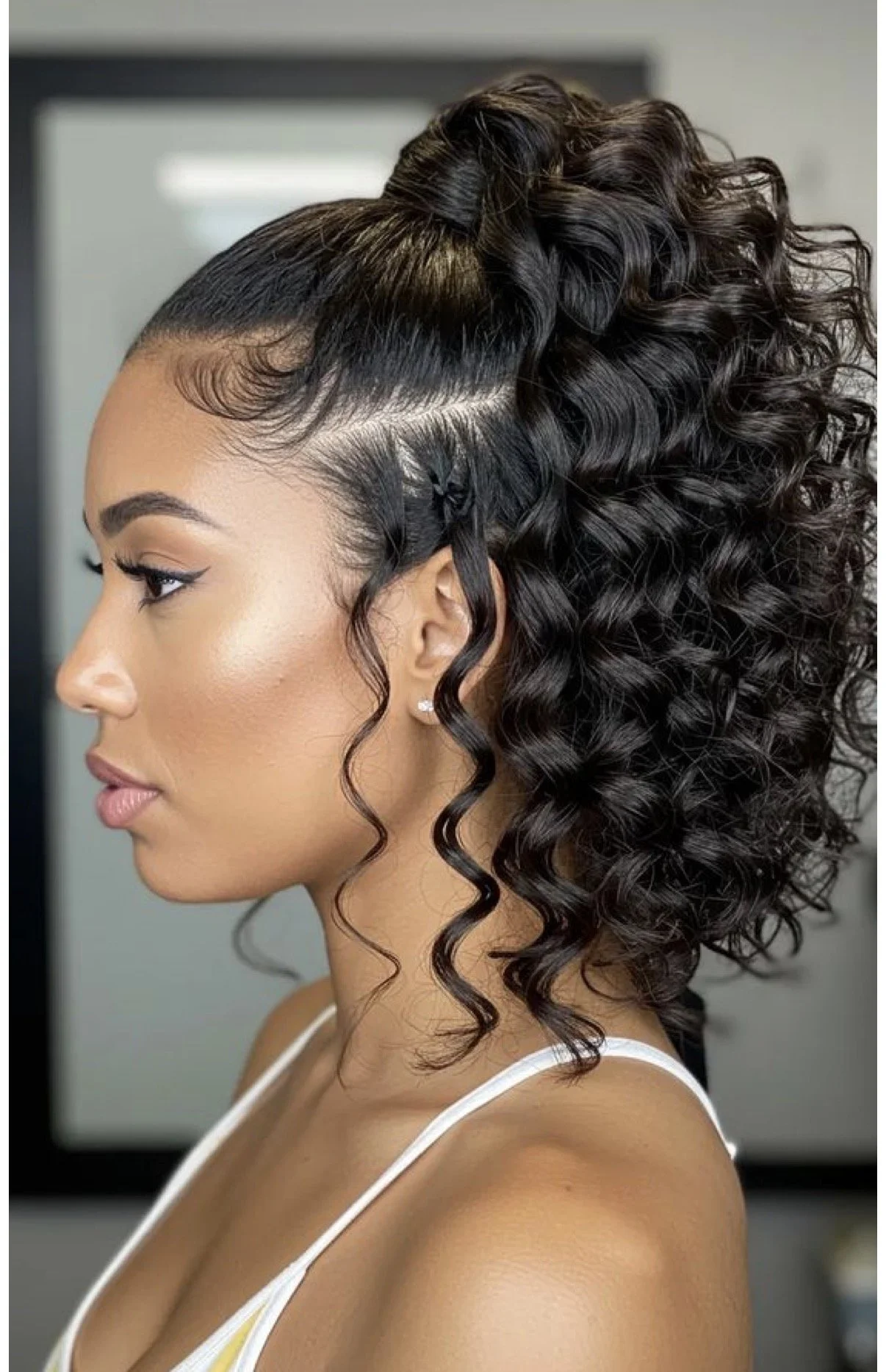 A woman with curly, styled hair pulled up on top with a side profile view.