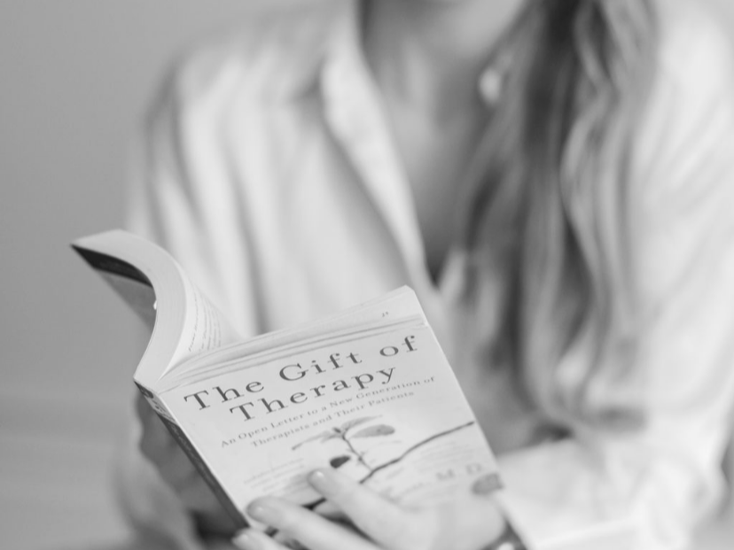 A person reading a book titled "The Gift of Therapy" in black and white photo.