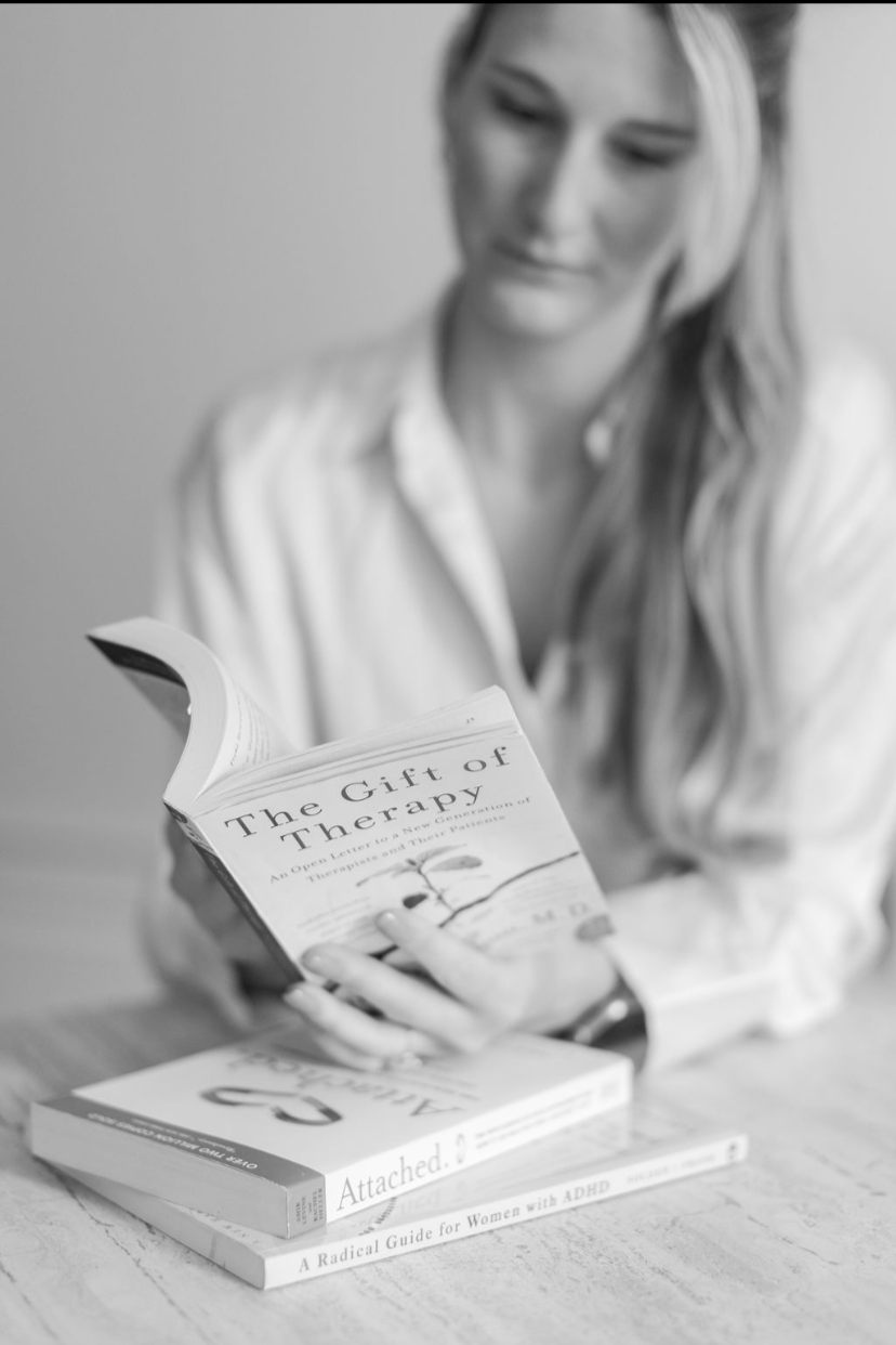 A woman with long hair reading a book titled 'The Gift of Therapy' in black and white.