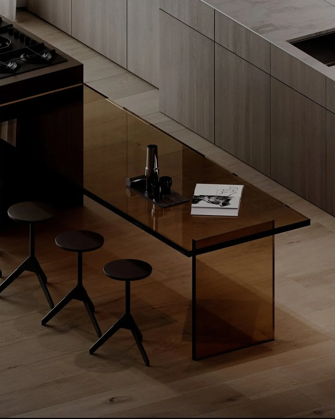 Une cuisine moderne avec un plan de travail en bois clair, des électroménagers intégrés, un café posé sur une table en verre sombre, ainsi qu’un magazine et une cafetière sur la table. Trois tabourets noirs en face de la table.