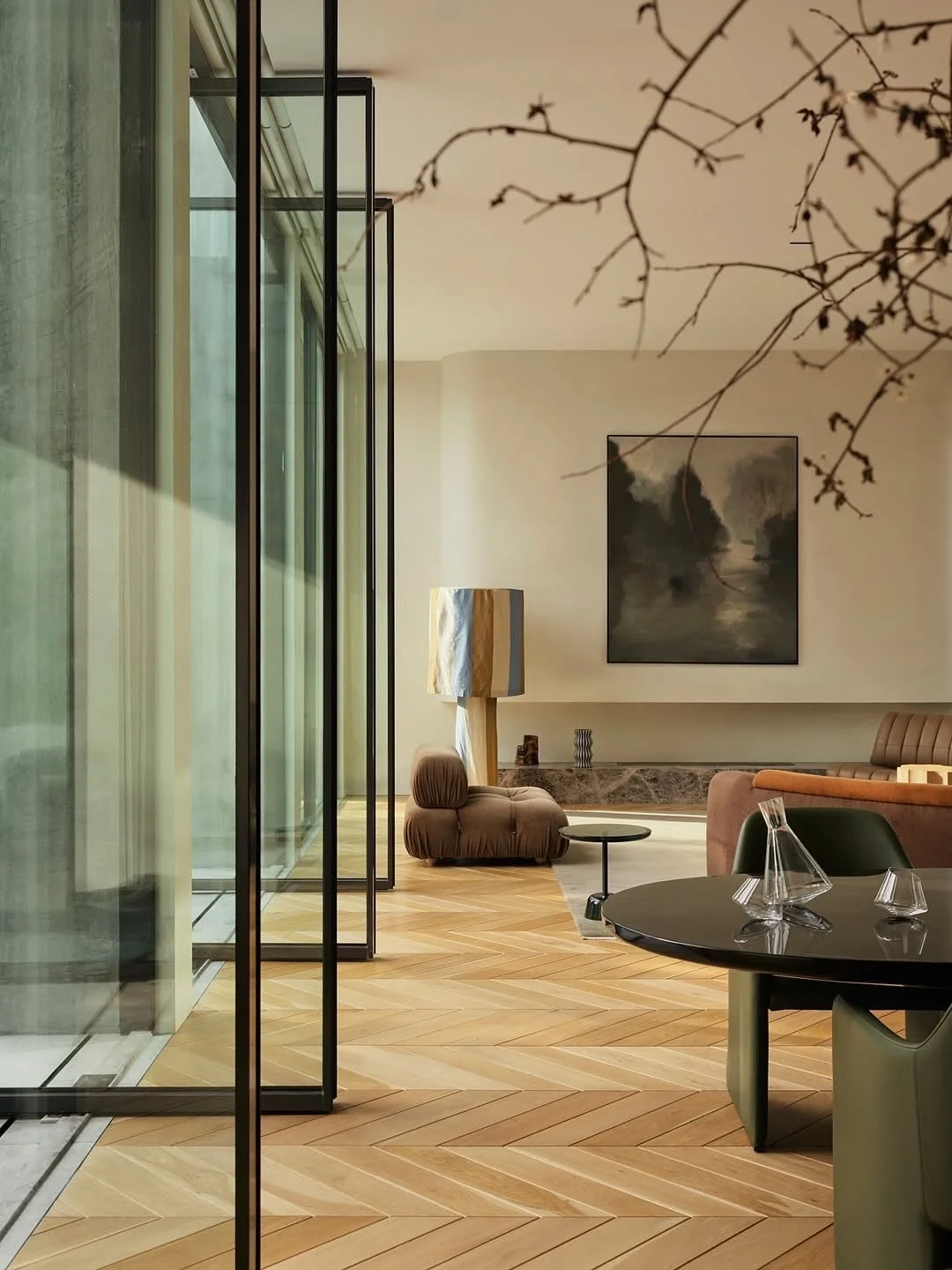 Intérieur d'un salon moderne avec mobilier aux tons neutres, un tableau prscene sur le mur, un lampadaire, et un grand vase en verre sur une table.