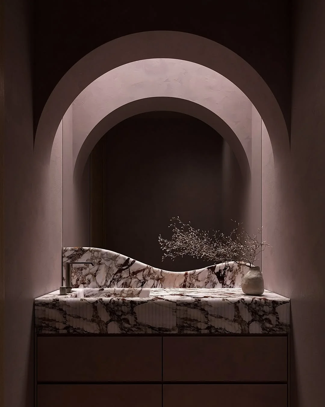 Lavabo en marbre avec un miroir en archet derrière, et une vase blanche avec des branches sèches sur le côté.