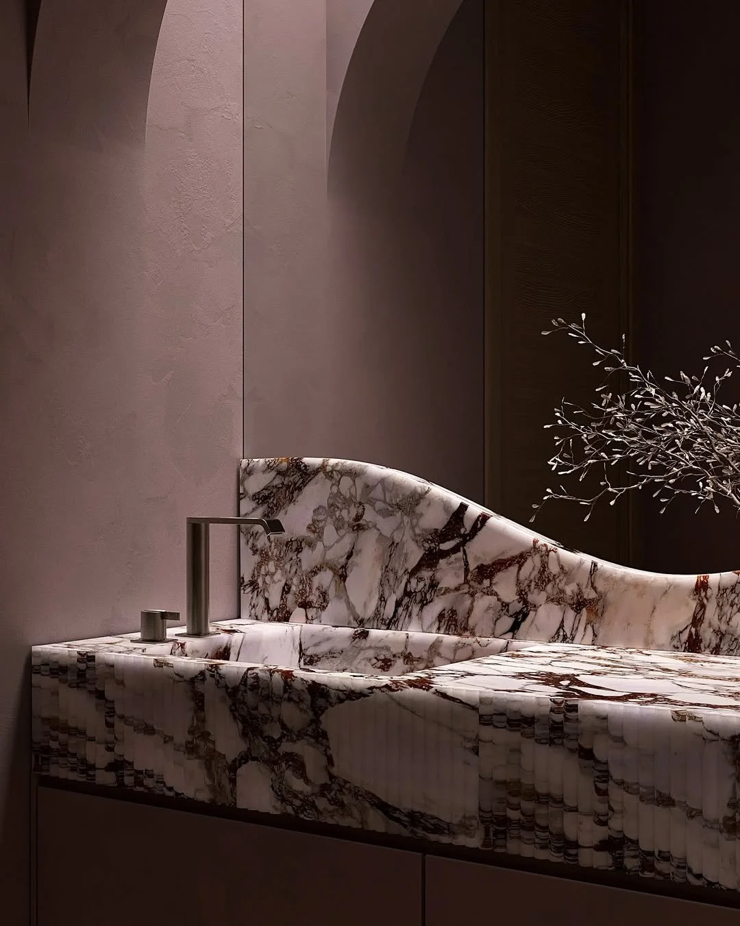 Lavabo en marbre blanc avec veins brunes, sur un meuble intégré, avec un robinet en métal et une branche sèche décorative à côté.