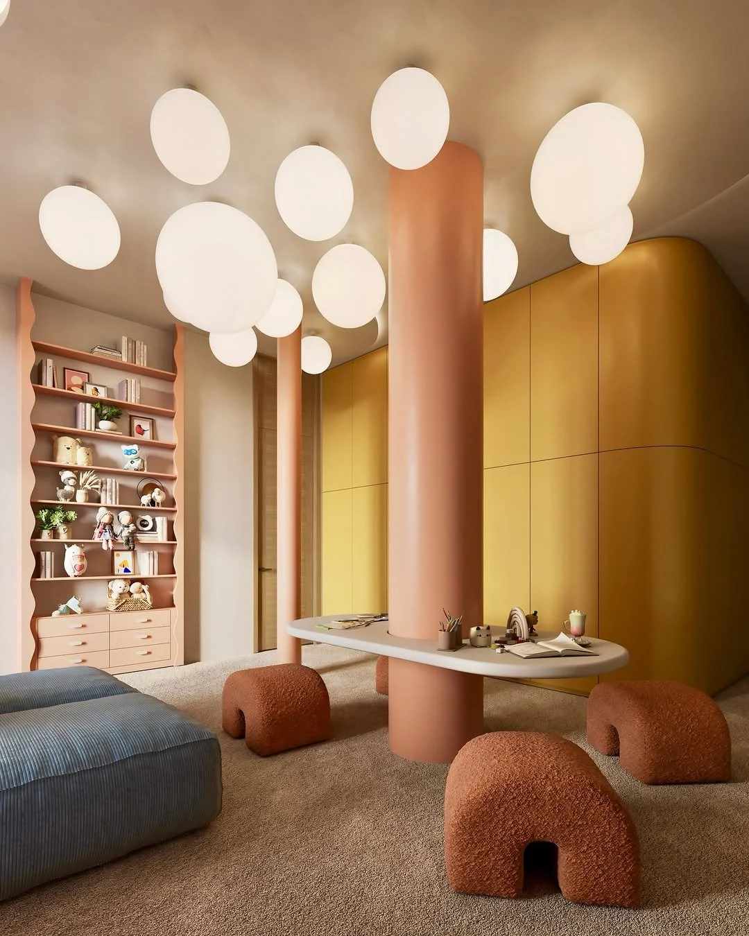 Intérieur d'une pièce moderne avec un plafond éclairé par plusieurs lampes blanches suspendues, une étagère avec des livres et des décorations, un mur jaune, un meuble rond avec des objets et des livres, et des sièges en forme de blocs arrondis en tissu