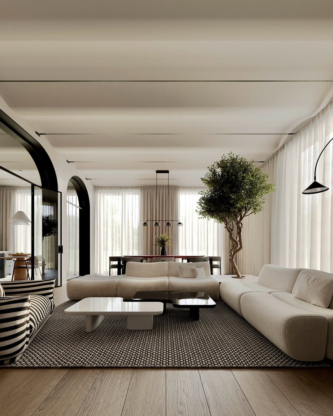 Salon moderne avec canapés blancs, tapis noir et blanc, table basse graphique, grande plante d'intérieur et grands rideaux blancs naturels.