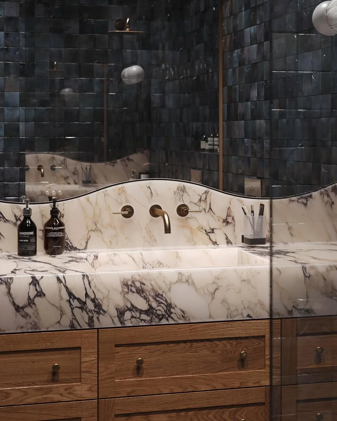 Un lavabo en marbre blanc avec des veines noires et dorées, situé dans une salle de bain élégante avec des murs en carreaux noirs brillants. Sur le lavabo, il y a deux bouteilles de savon, un porte-ustensiles avec des brosses et un miroir en verre.